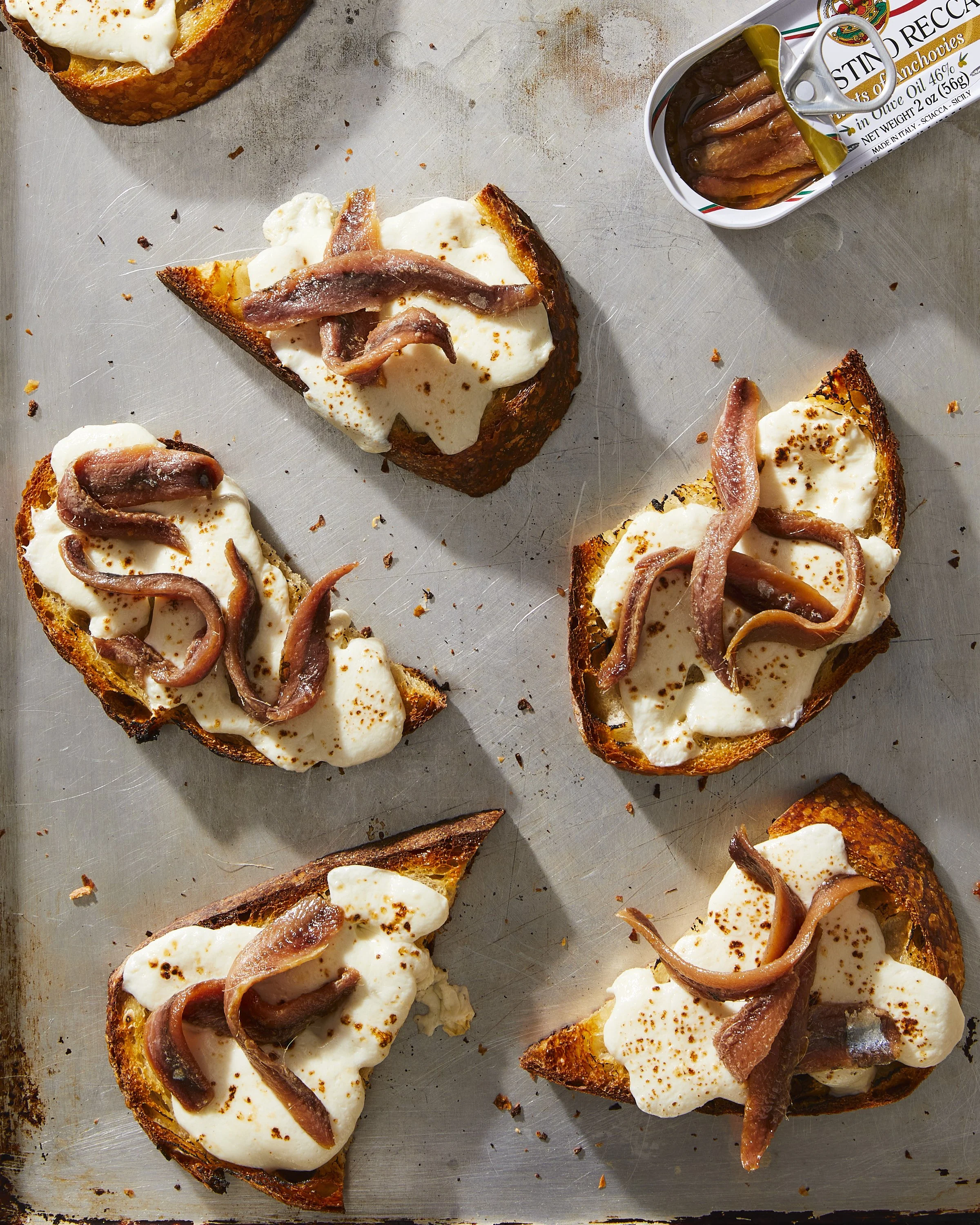A surface of toasted crostini with melted mozzarella and anchovies on top, photographed by Julia Gartland for The Kitchn - food styling, commercial food stylist NYC