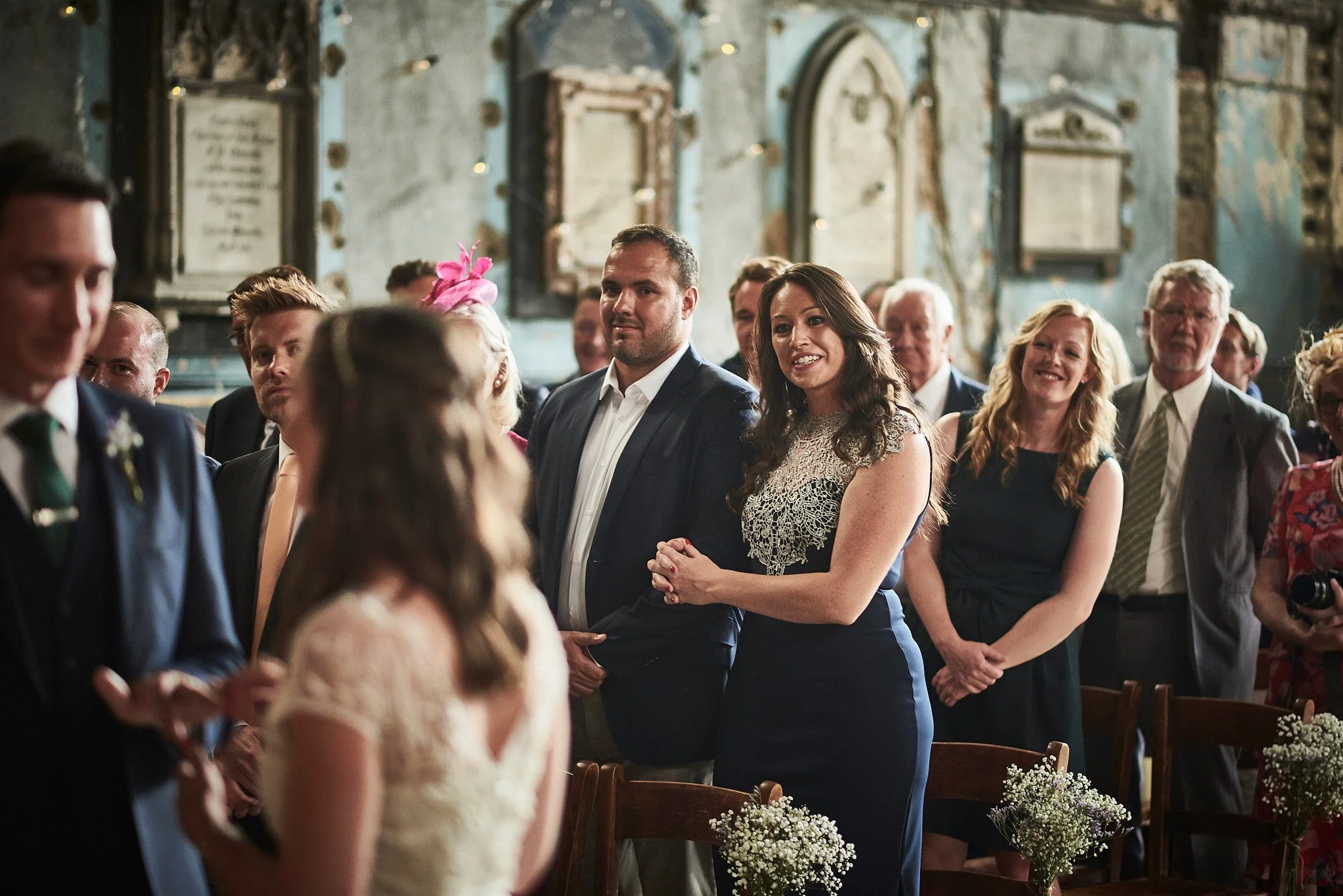 People attending a wedding ceremony inside a church, with some smiling and watching the couple at the altar.