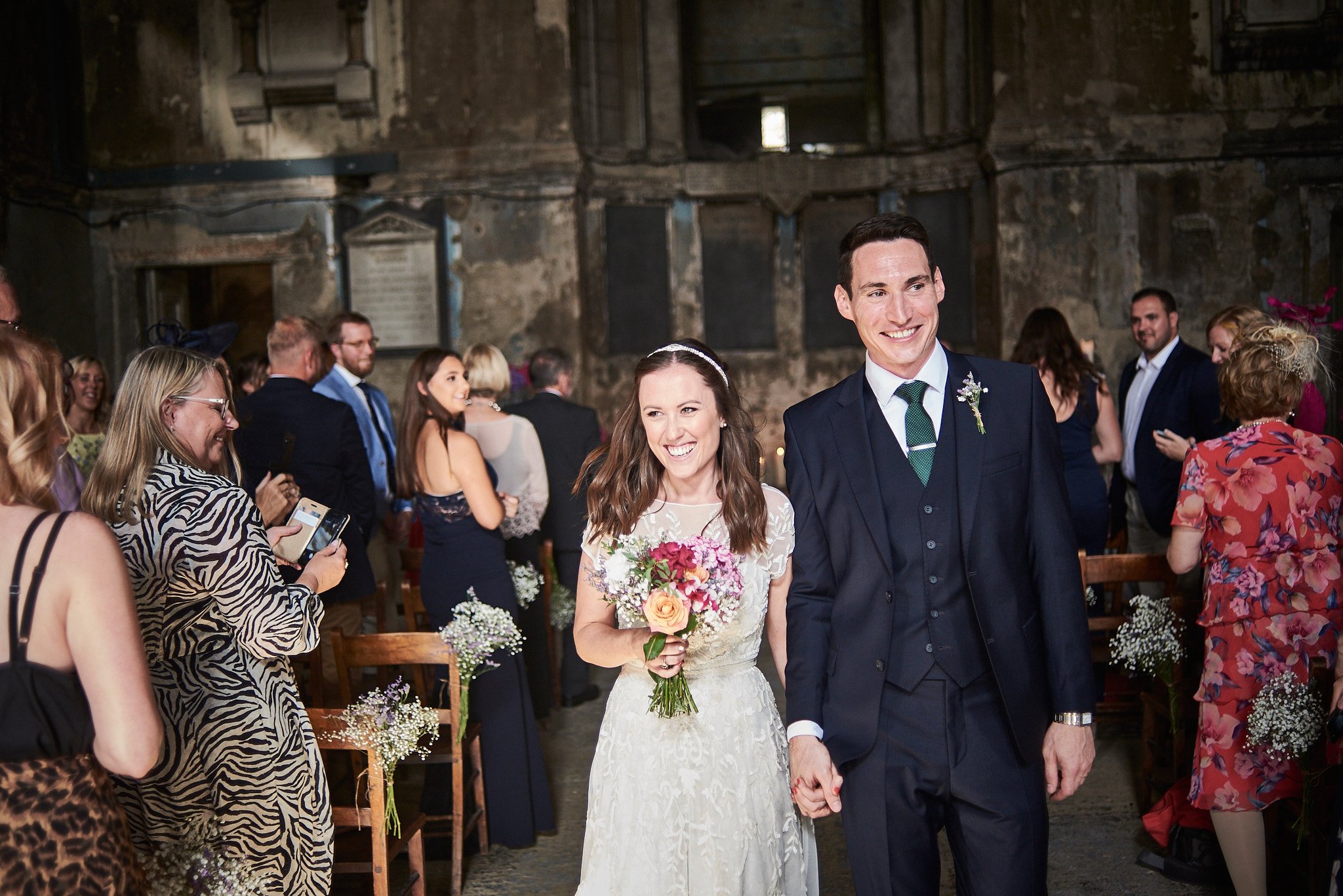 Happy bride and groom holding hands walking down the aisle during their wedding ceremony, surrounded by guests.