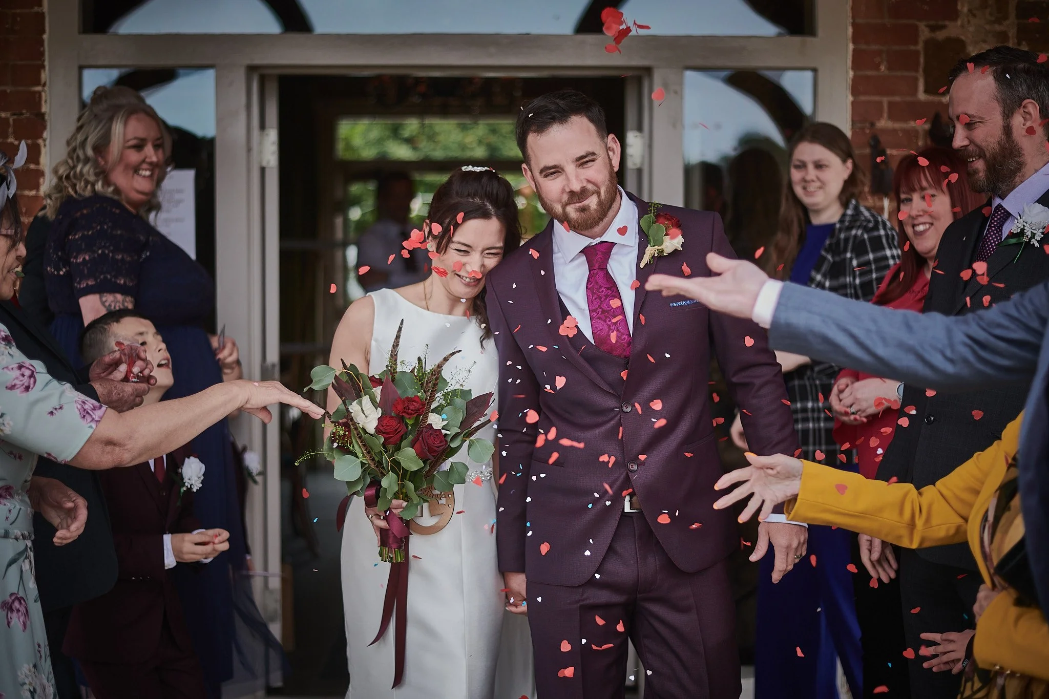 Bride and groom walking through confetti with friends and family celebrating.