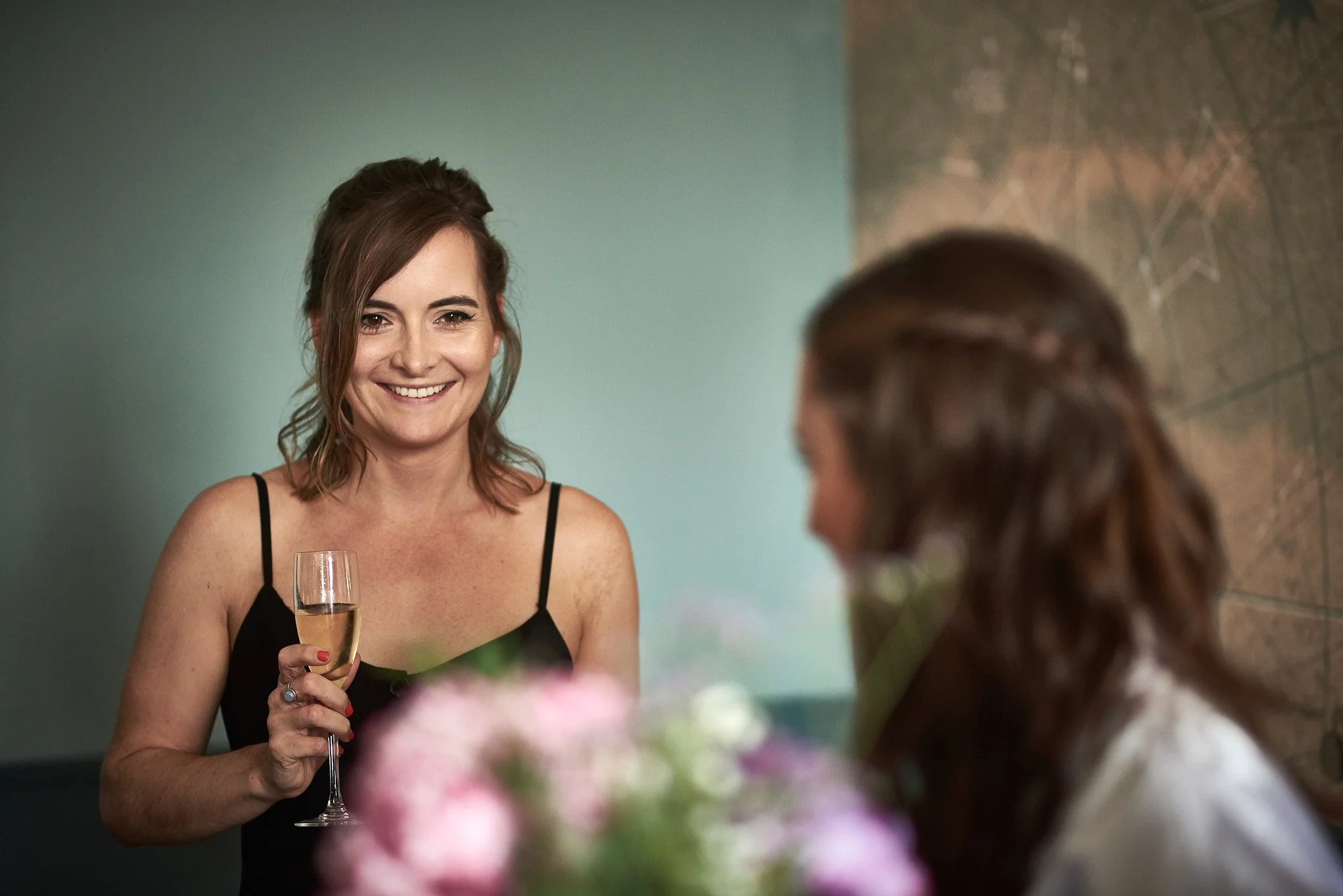 A woman in a black dress smiling and holding a glass of champagne at a social gathering.