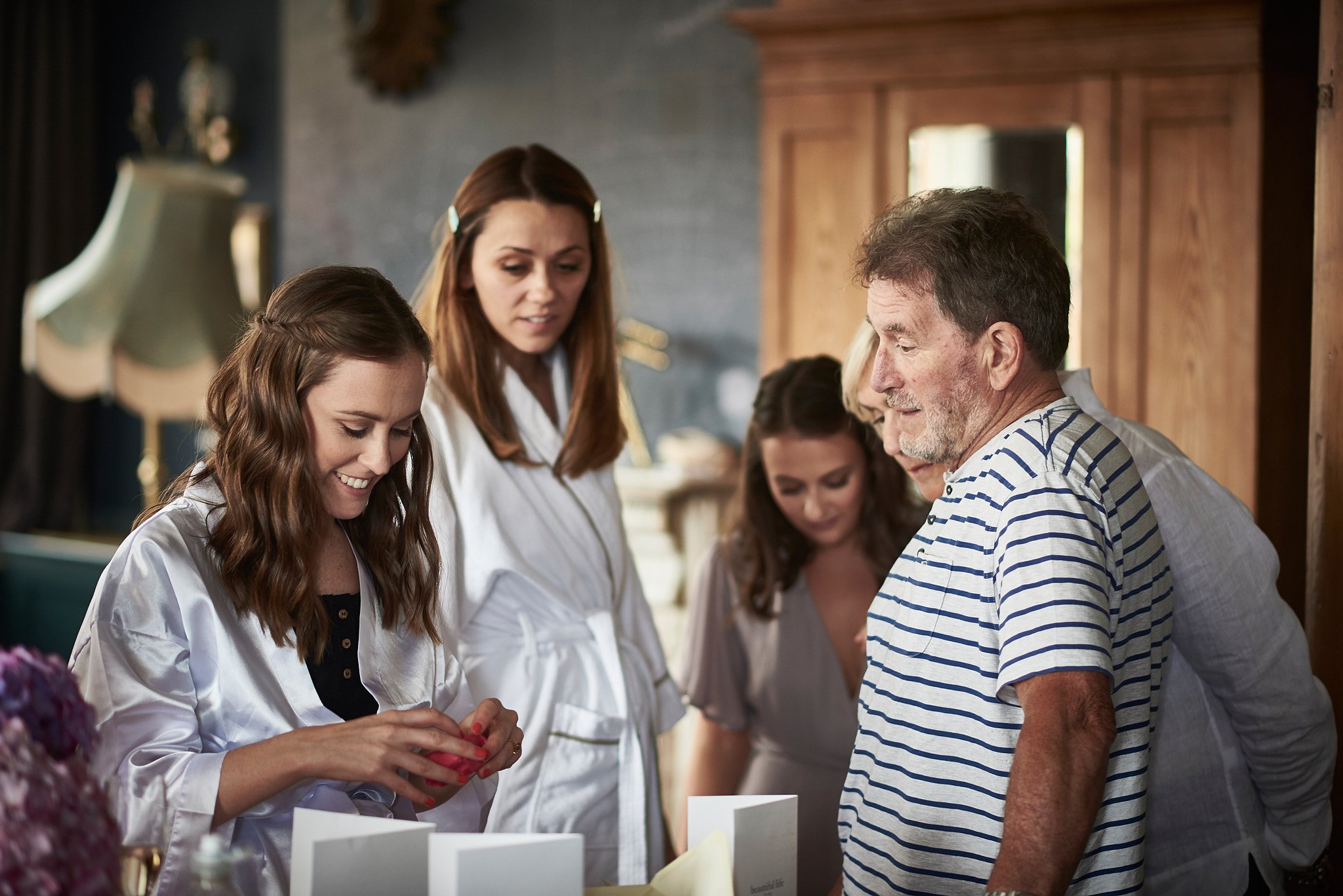 Group of women and an older man examining items on a table in a cozy, well-lit room.