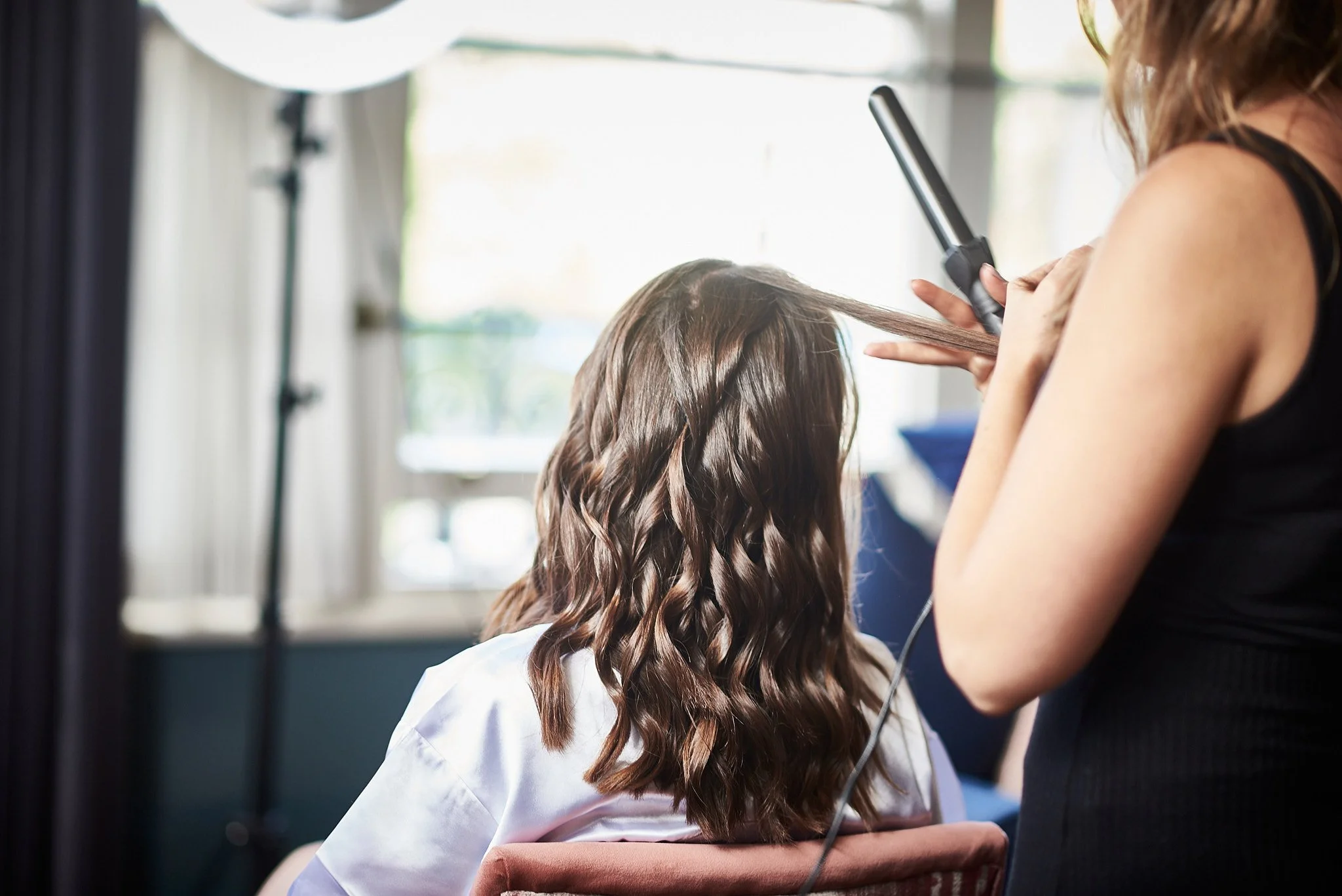 A hairdresser flat-ironing a woman's wavy hair in a salon.