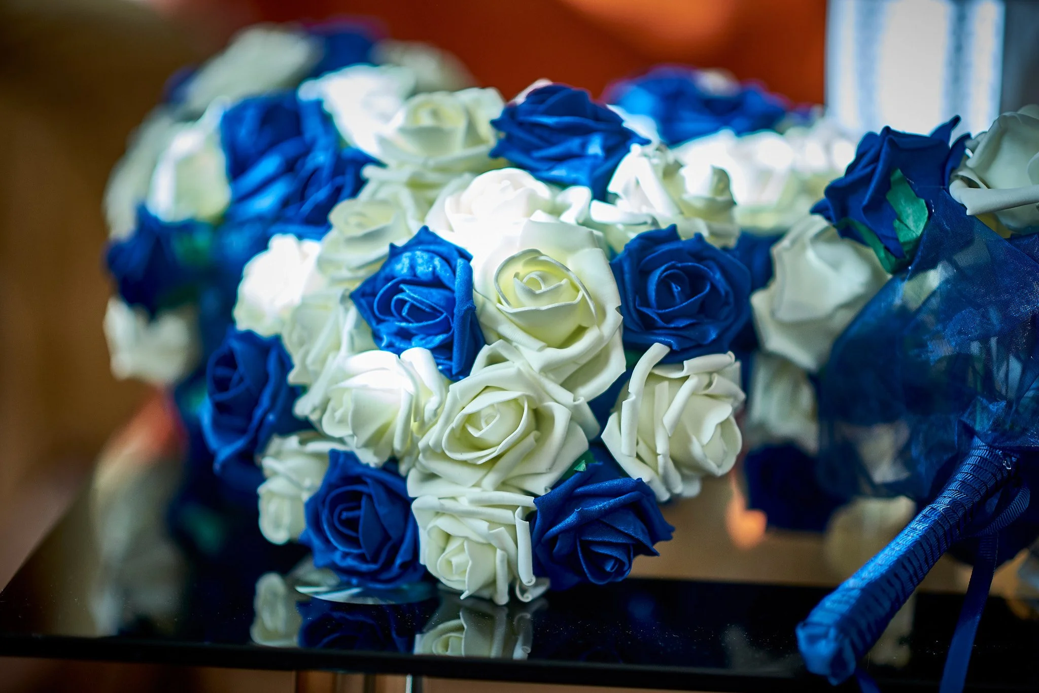 Bouquet of artificial blue and white roses with a wrapped handle, placed on a reflective surface.