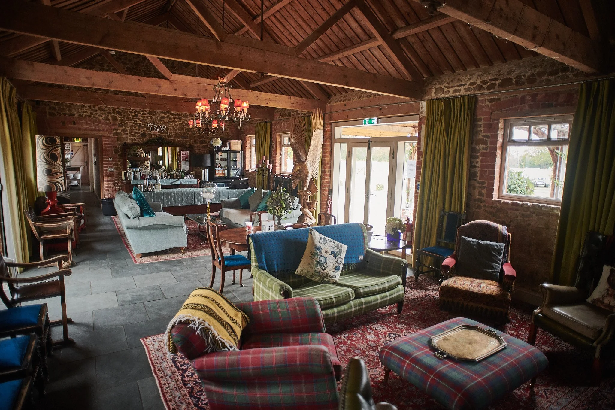 Interior of a cozy lounge area with vintage furniture, exposed brick walls, green curtains, a chandelier, and a bar in the background.