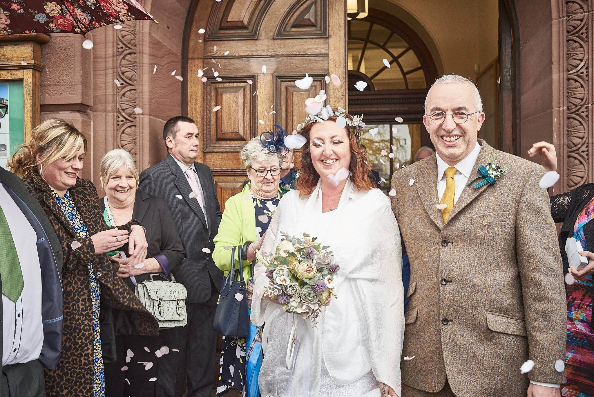 A bride and groom celebrating with friends and family outside a church, with confetti falling around them.