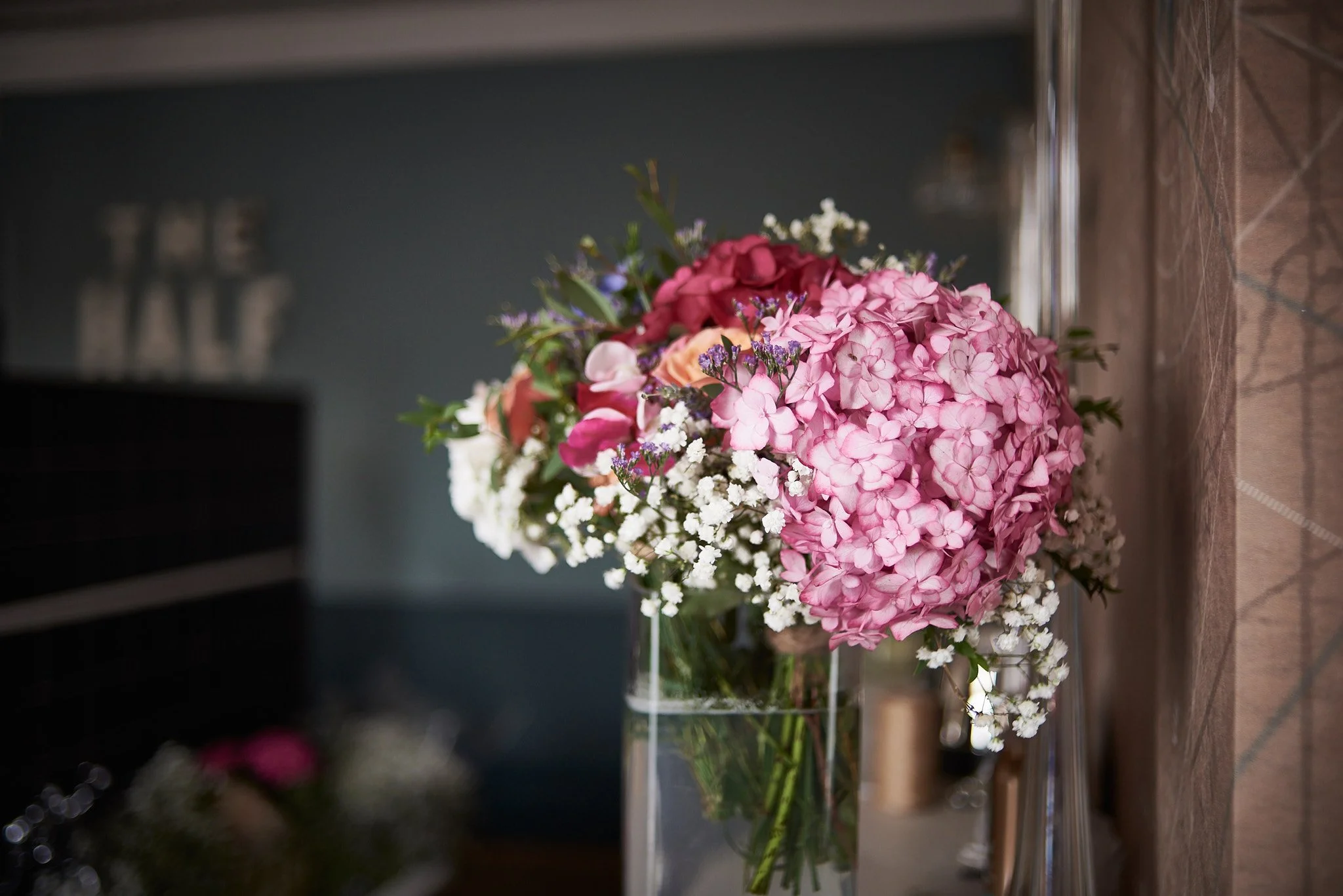 A bouquet of pink hydrangeas, white baby's breath, and other colorful flowers in a glass vase on a kitchen countertop.
