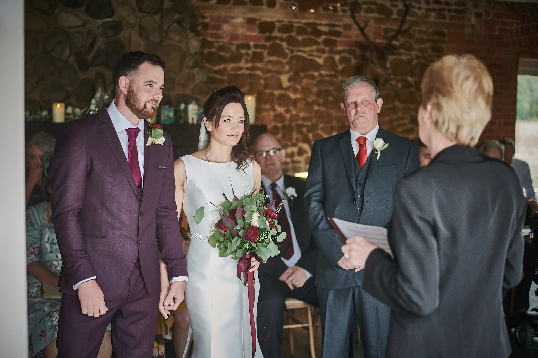Bride and groom exchanging vows at wedding ceremony with officiant, in a rustic venue with stone walls