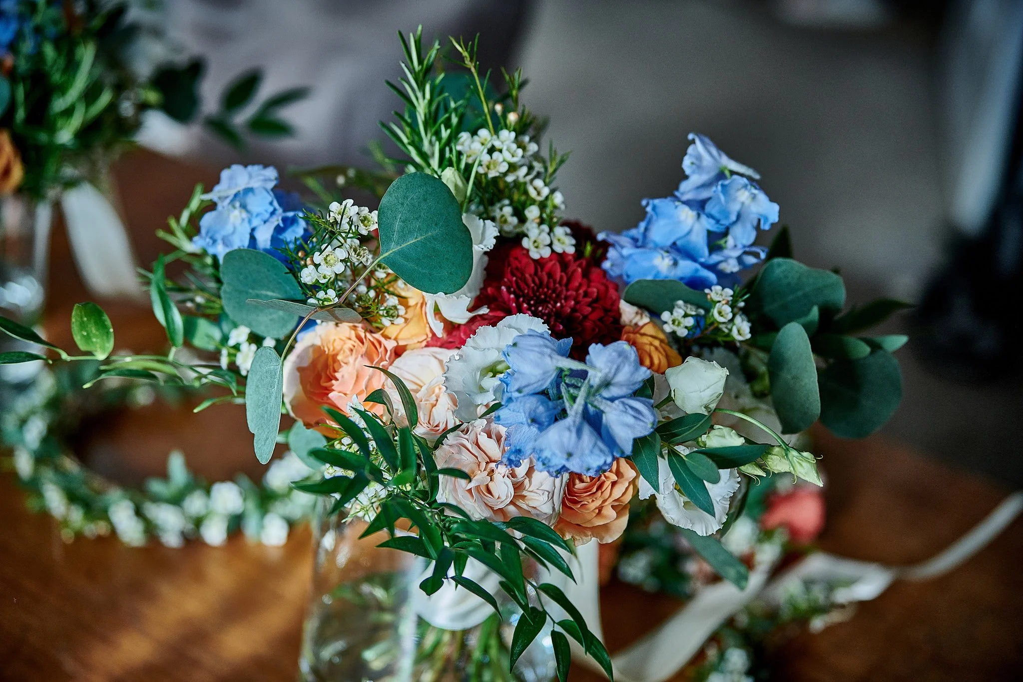 A bouquet of colorful flowers including blue, red, peach, and white roses, accented with green foliage, in a glass vase on a wooden surface.