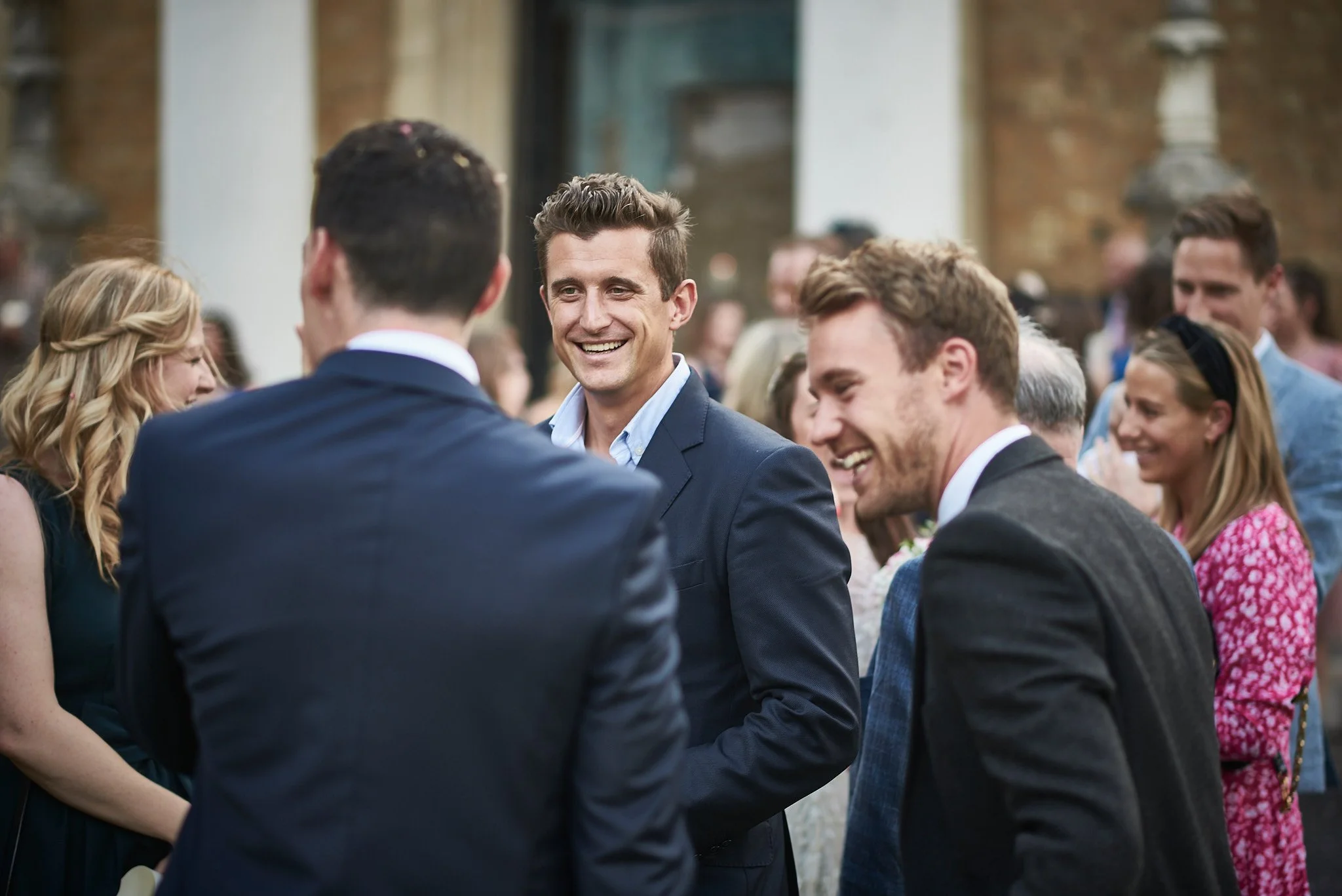 People at a social gathering, smiling and chatting, outdoors in a casual setting.