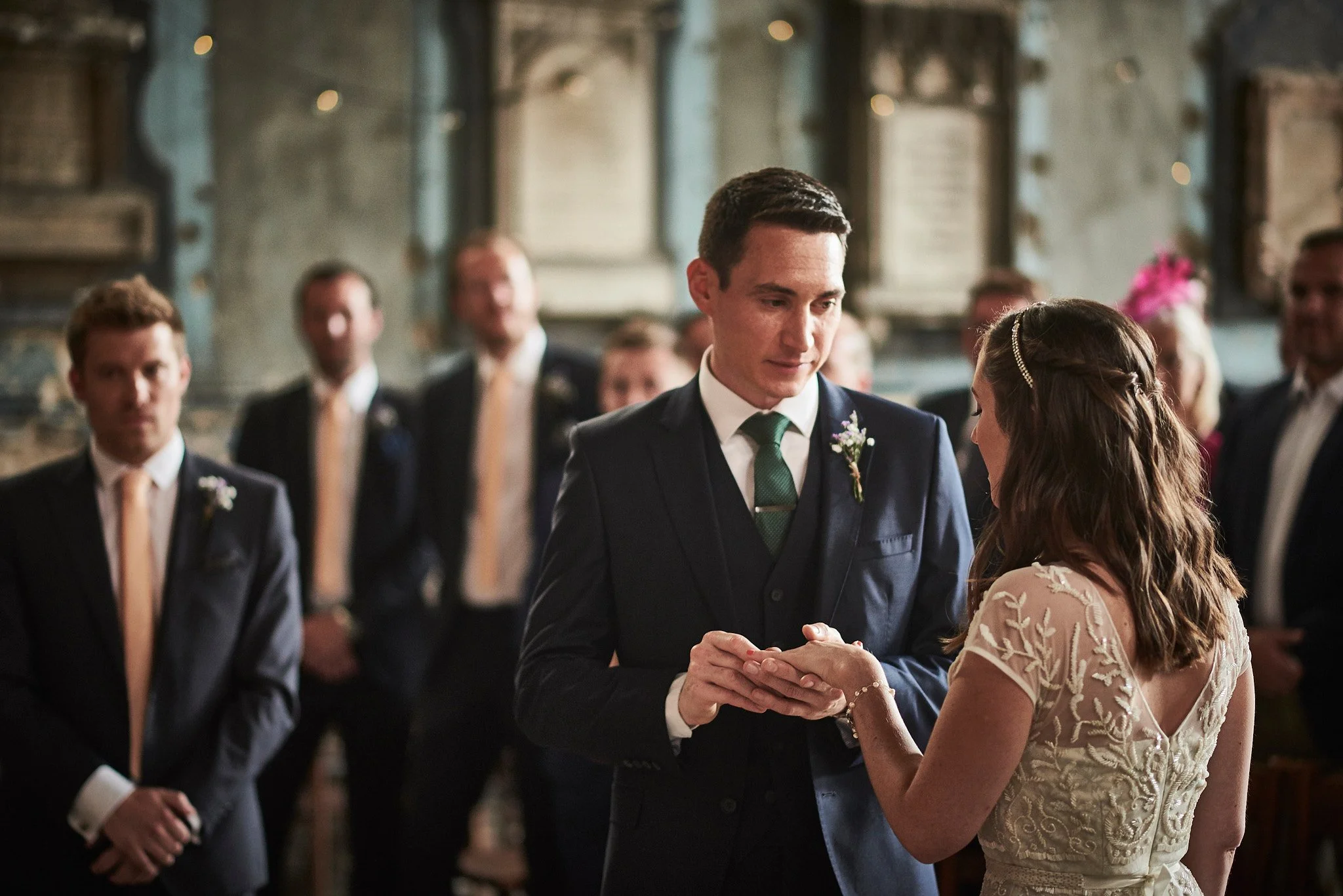 A couple exchanging rings during a wedding ceremony in a historic church with family and friends witnessing.