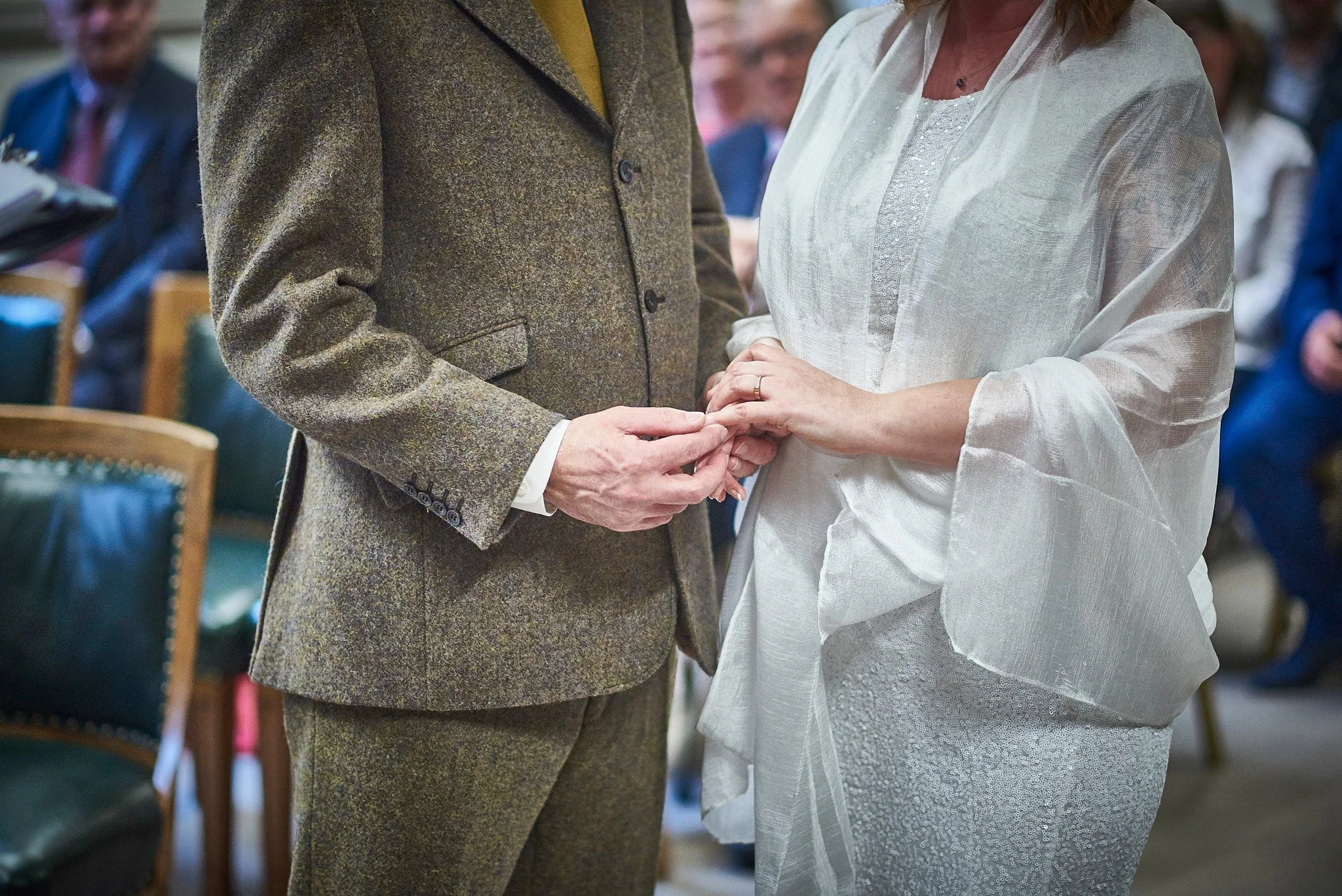 Couple exchanging wedding rings during a ceremony, focusing on their hands and attire.