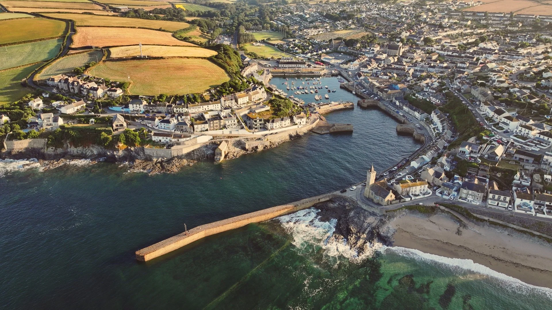 Aerial view of Porthleven Harbour filled with boats and surrounded by houses, cliffs, and green fields.