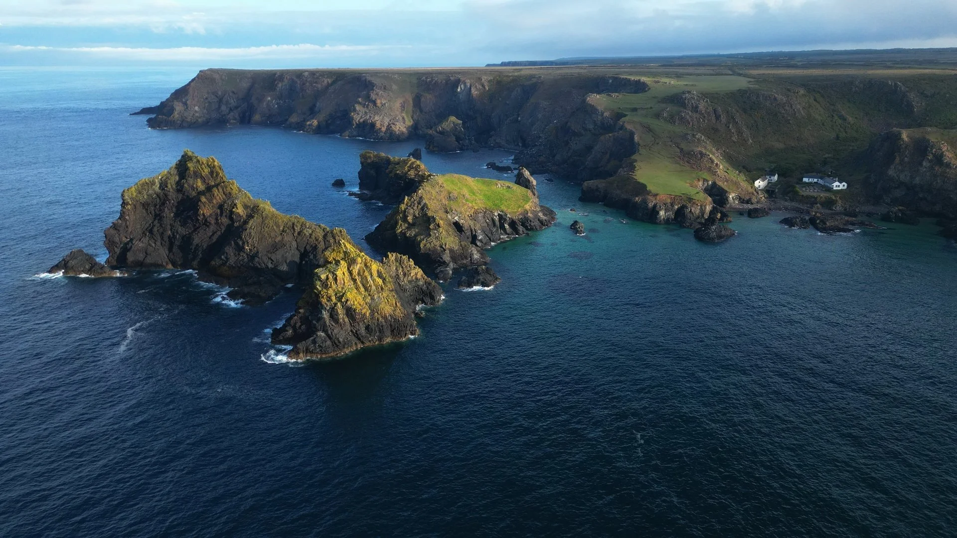 Aerial view of Kynance Cove in Cornwall showing rugged cliffs, rock formations, turquoise water and the surrounding coastline.