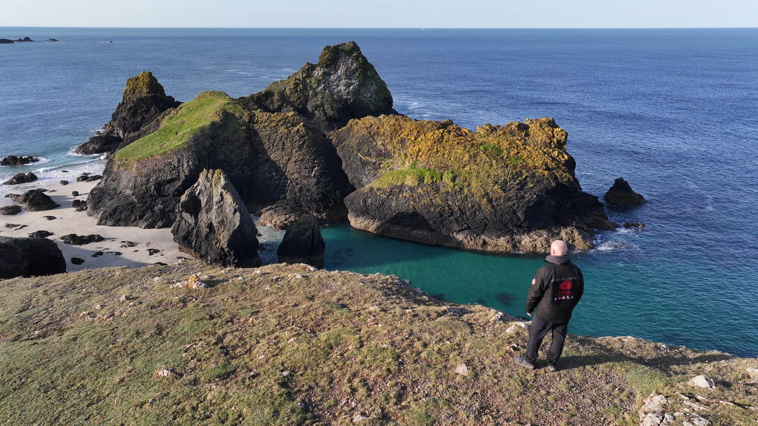 A landscape image of a man standing looking as the view at Kynance Cove