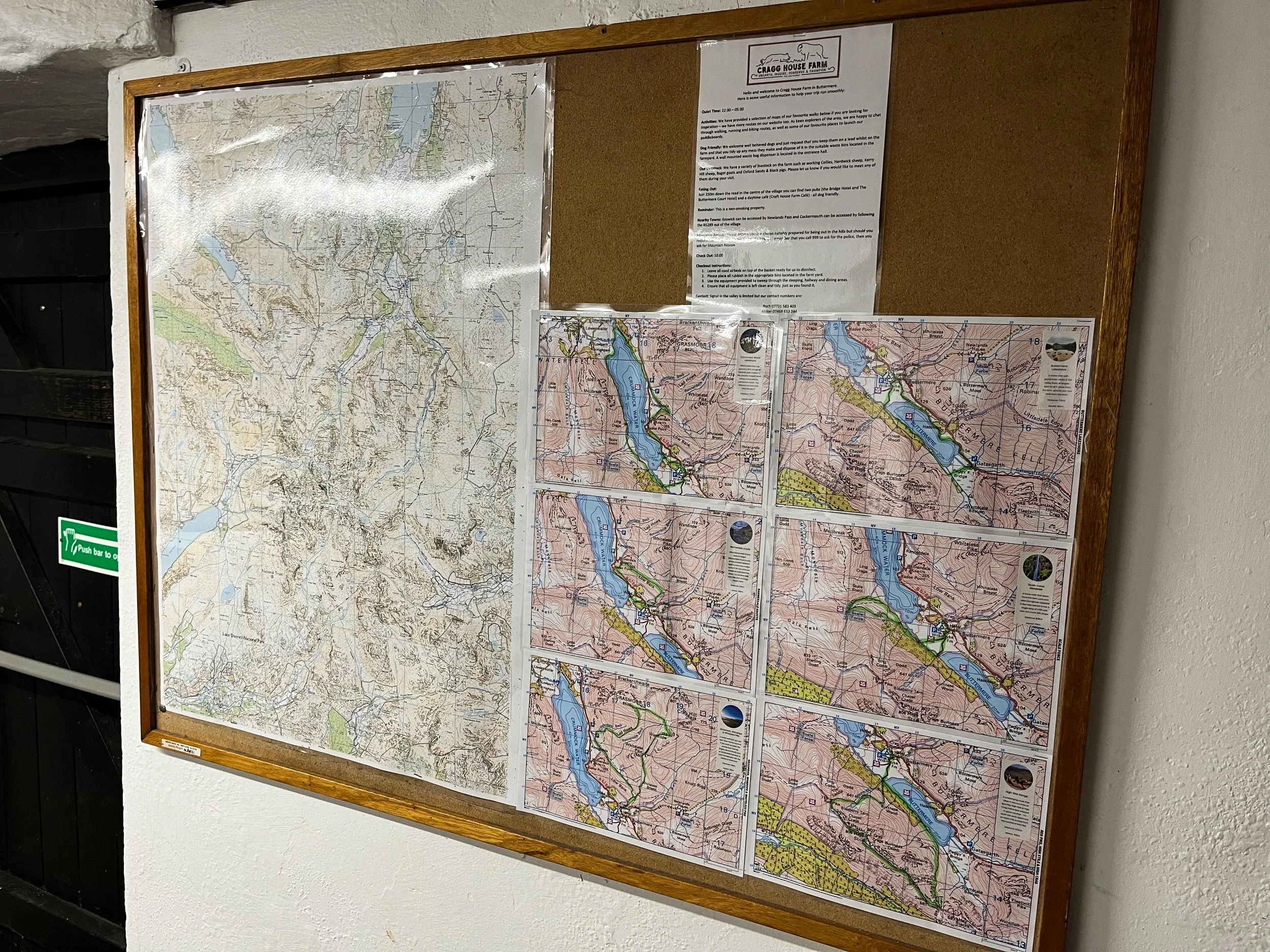 A bulletin board with a large map on the left and smaller maps on the right, along with a notice at the top, all within a wooden frame, mounted on a wall.