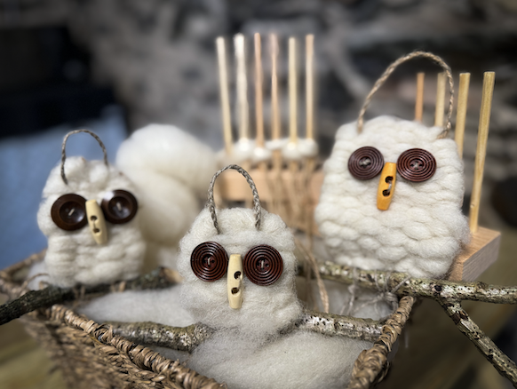 Handmade owl decorations with curly brown eyes and button noses, made of white fluffy material, displayed in a wicker basket and on a wooden surface.