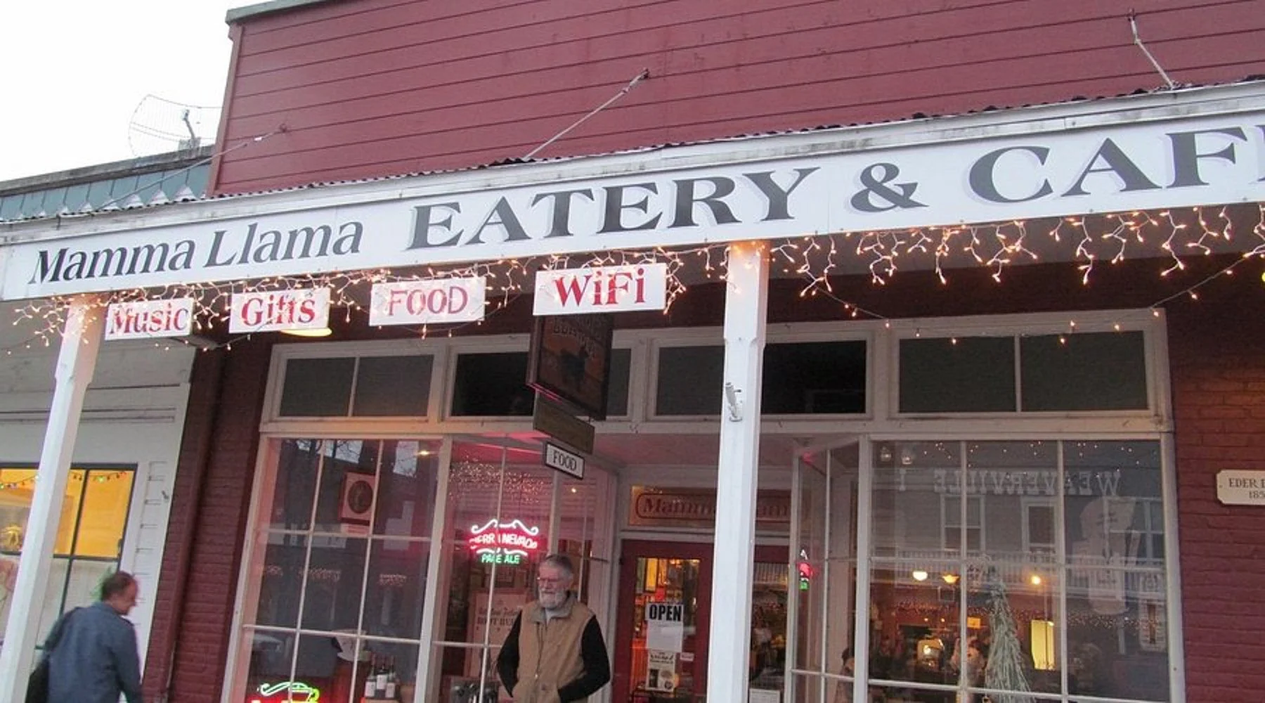 Exterior of Mamma Llama Eatery & Cafe with signboard, string lights, and two people standing outside.