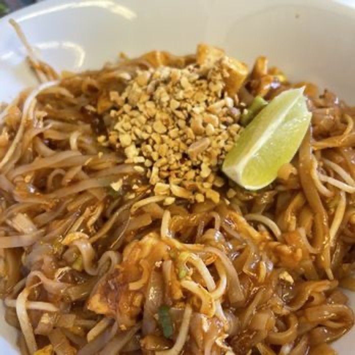 Plate of Pad Thai noodles topped with crushed peanuts and a lime wedge.