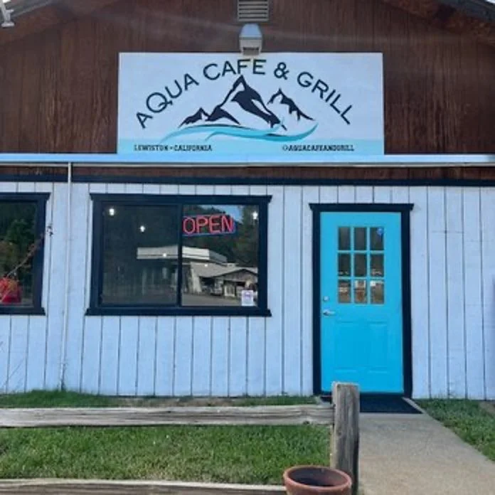 Exterior of Aqua Cafe & Grill with a blue door, a window with an "Open" sign, and a sign with mountains and water indicating the location in Livestock, California.