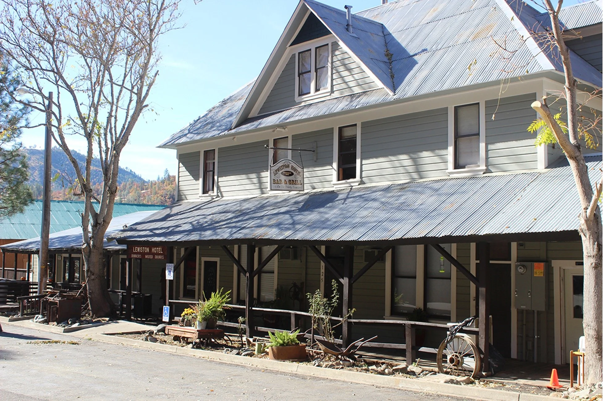 Historic three-story building with a metal roof, sign reading 'Lewiston Hotel,' and outdoor seating area, surrounded by trees and mountainous landscape in the background.