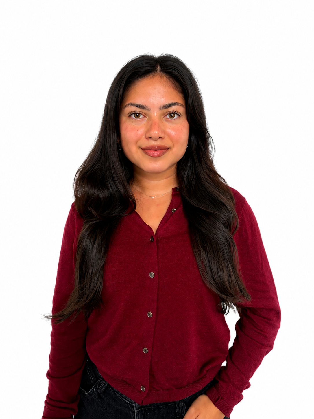 A woman with long dark hair wearing a red cardigan and black pants standing against a white background.