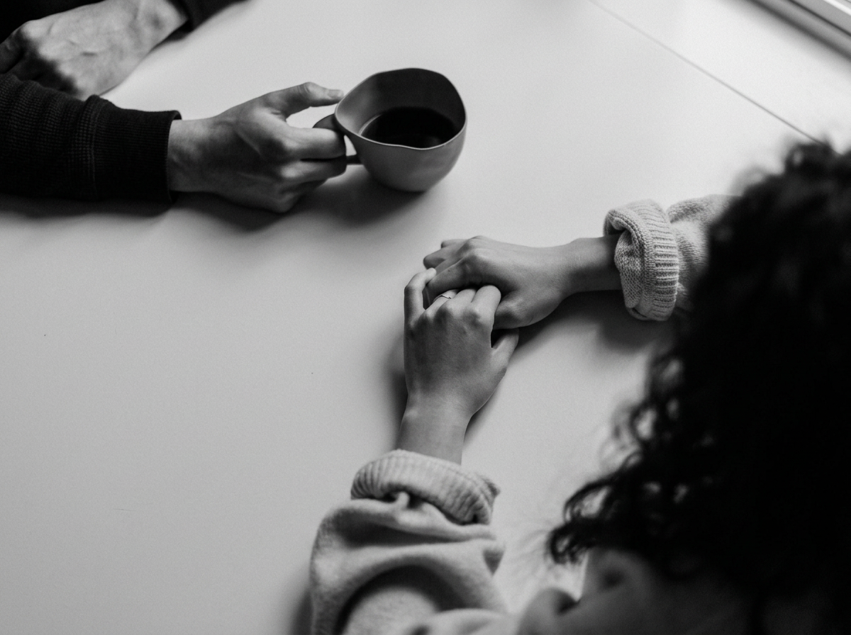 Two people holding hands across a table, with one holding a mug.