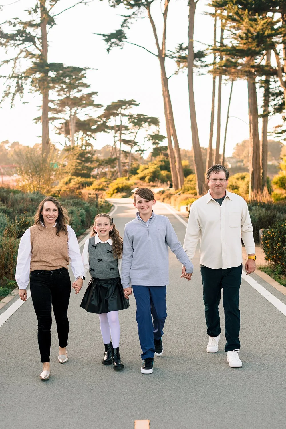 A family of five walking down a scenic path in a park during sunset, holding hands and smiling.