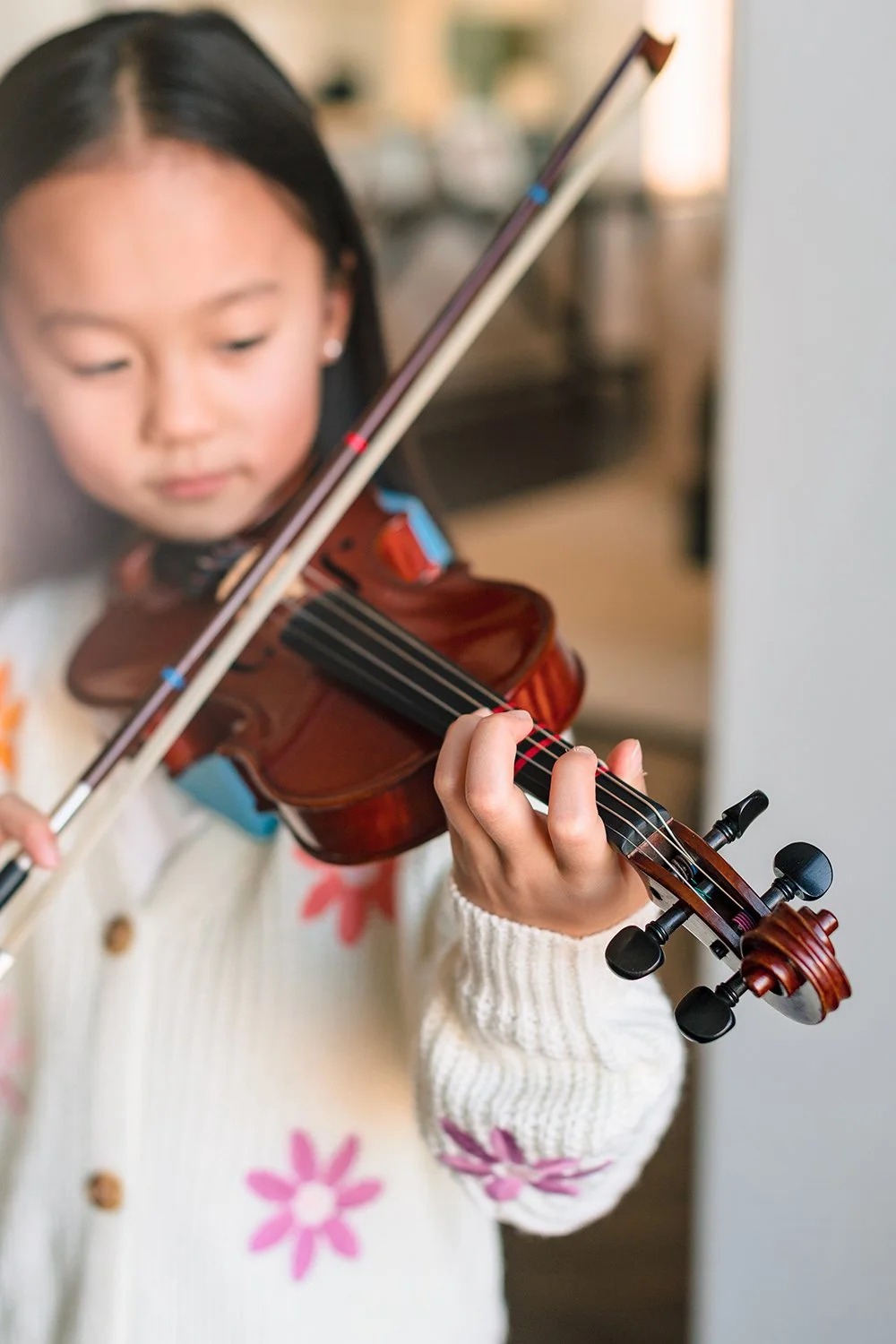 Young girl playing a wooden violin with a bow, indoors.