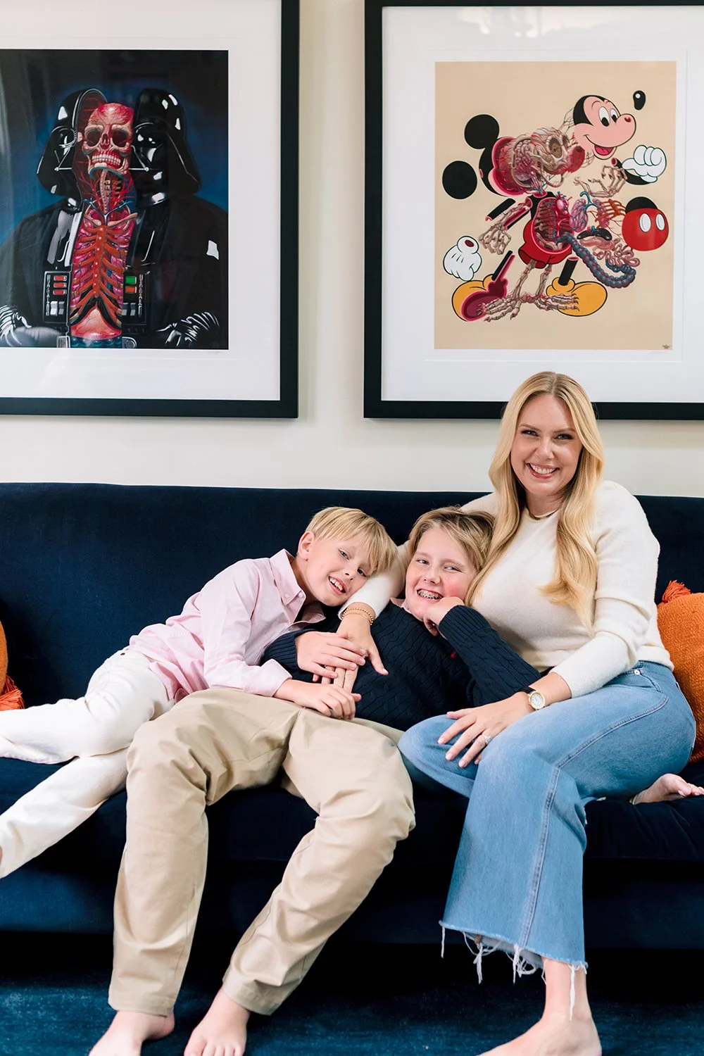 A family of three sitting on a navy blue sofa, smiling and hugging, in a room with framed artwork of Darth Vader and Mickey Mouse on the wall behind them.