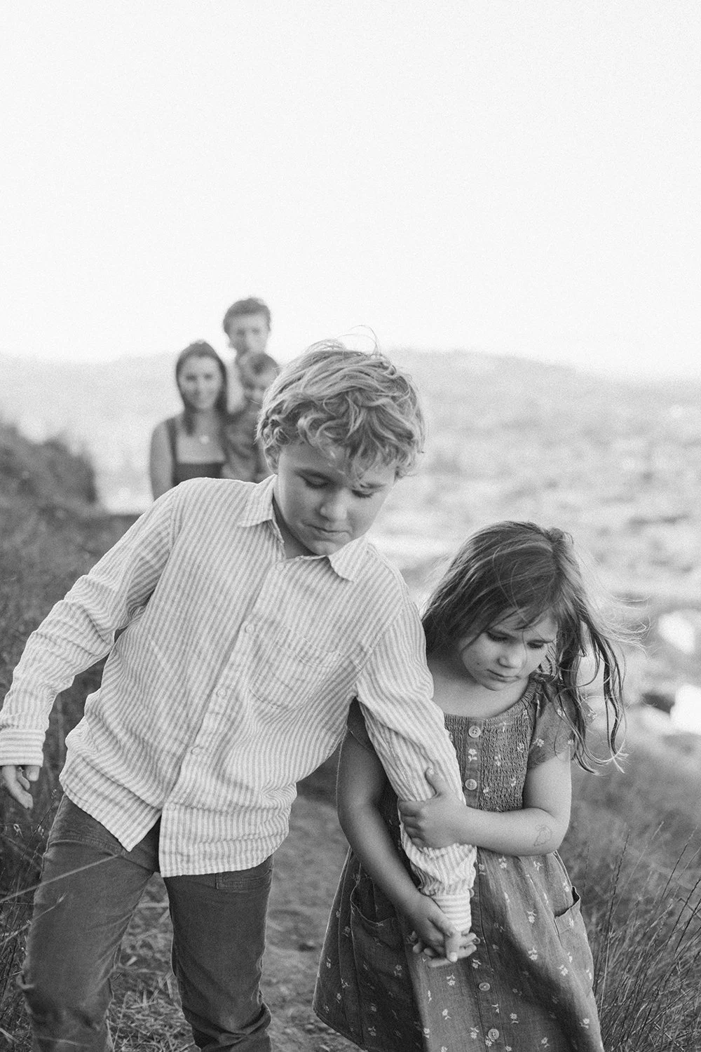 A group of children walking outdoors on a windy day, with two children in front, one boy and one girl, and two more children in the background, walking behind them.