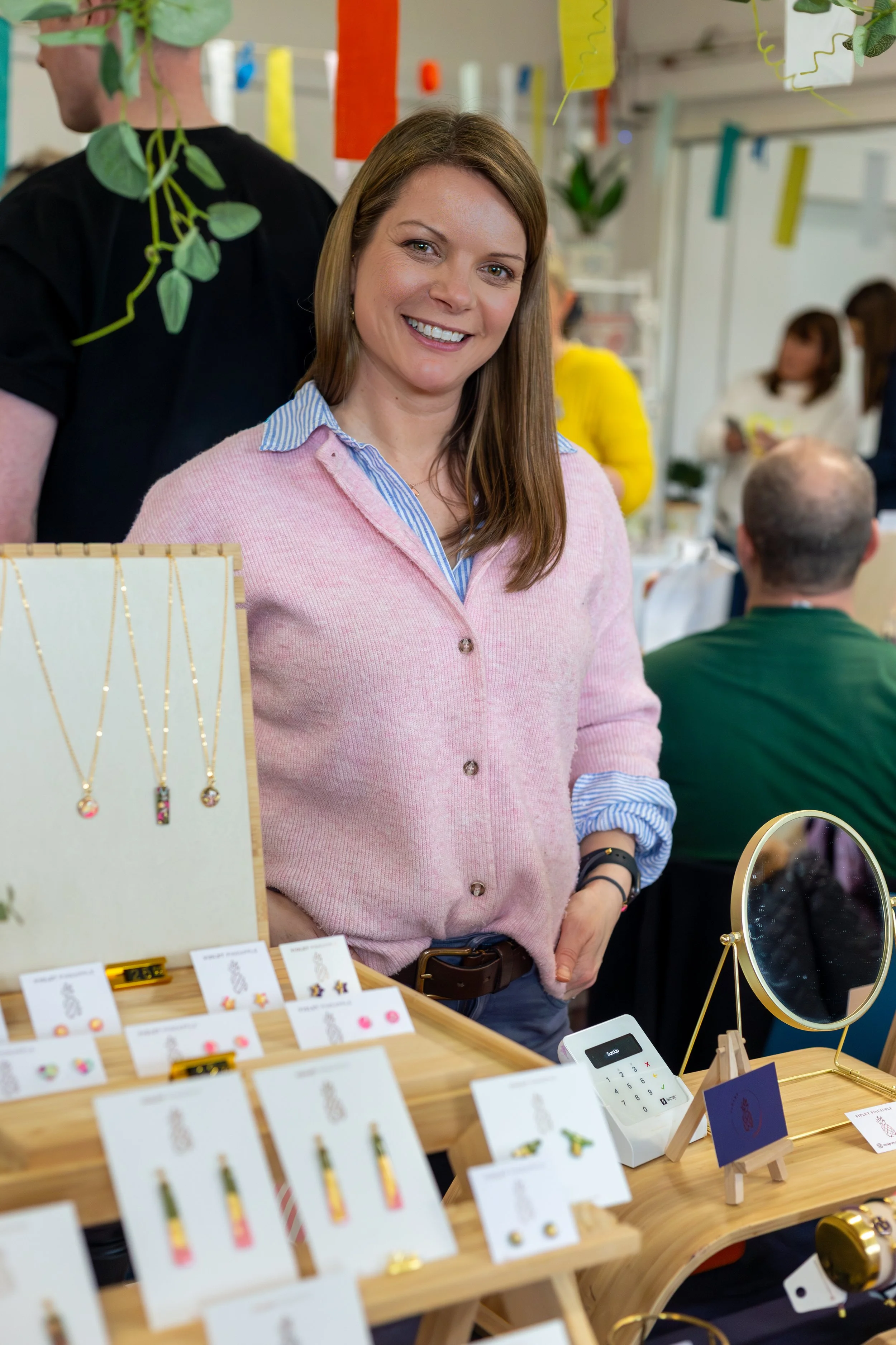 Independent jewellery maker smiling behind her stall at a Paper Daisy makers fair, with colourful handmade earrings and necklaces on display