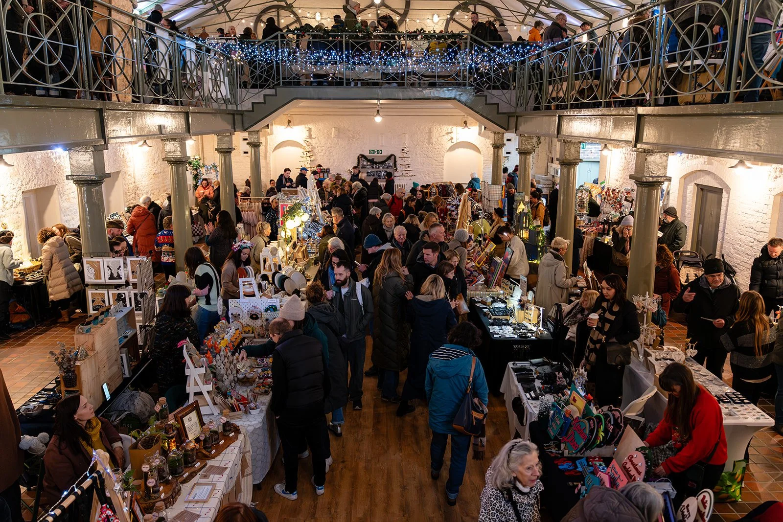 Independent jewellery maker smiling behind her stall at a Paper Daisy makers fair, with colourful handmade earrings and necklaces on display