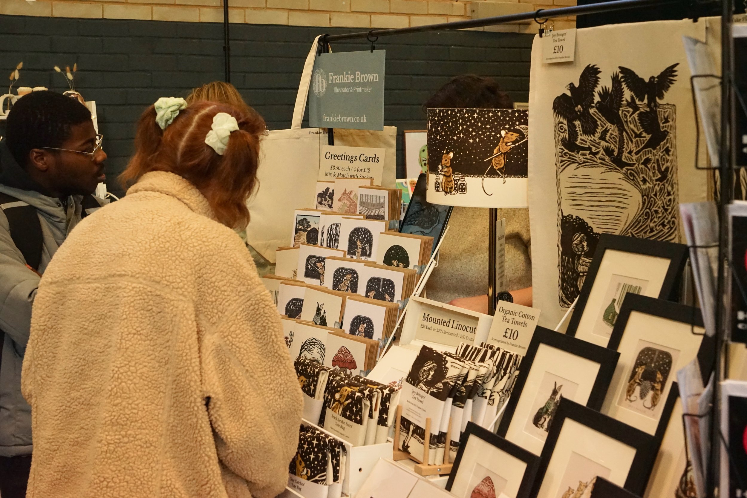 Independent artist stall with visitor at a Paper Daisy makers fair, with colourful handmade earrings and necklaces on display