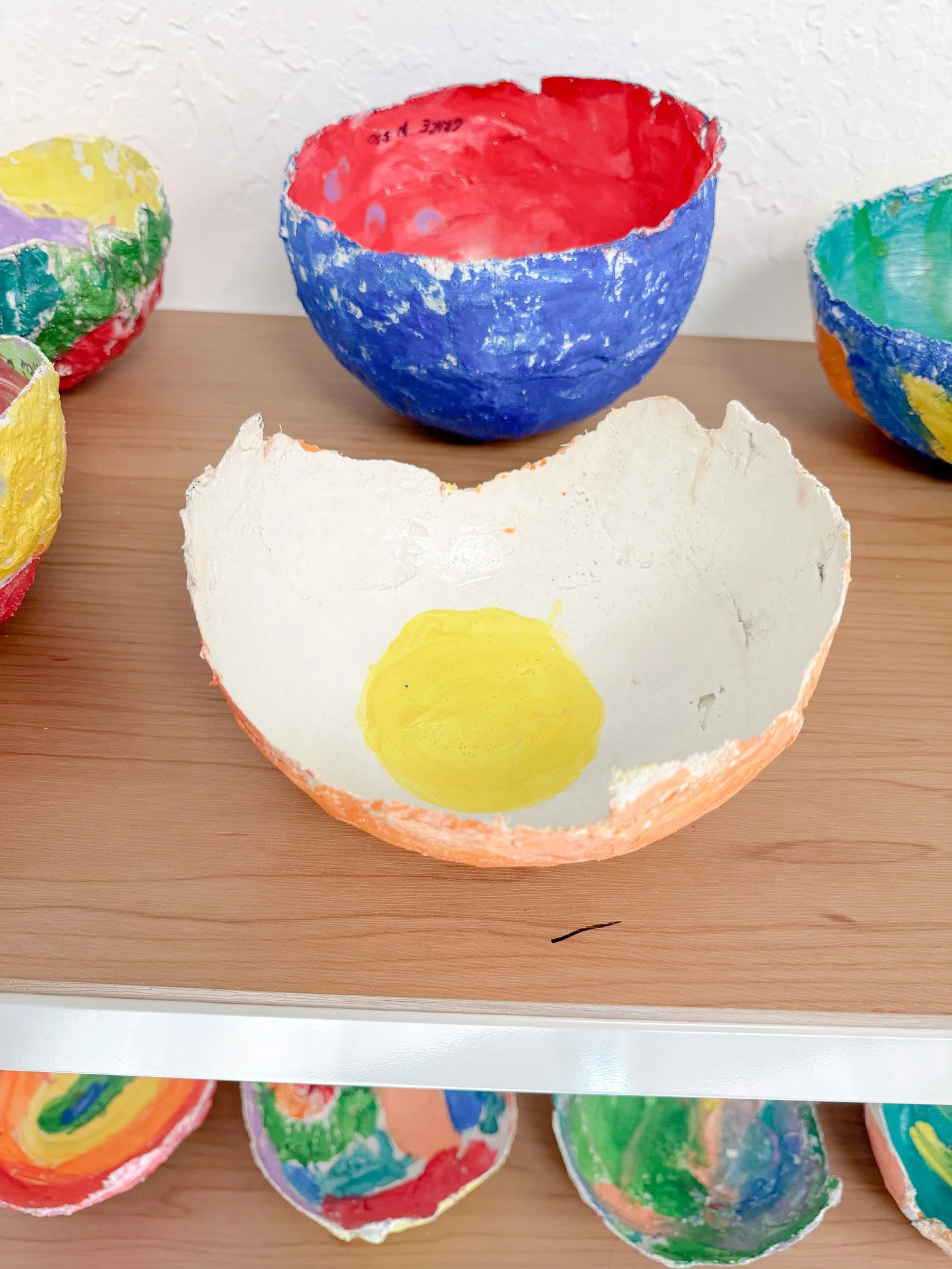 Colorful, painted eggshell bowls on wooden shelves.