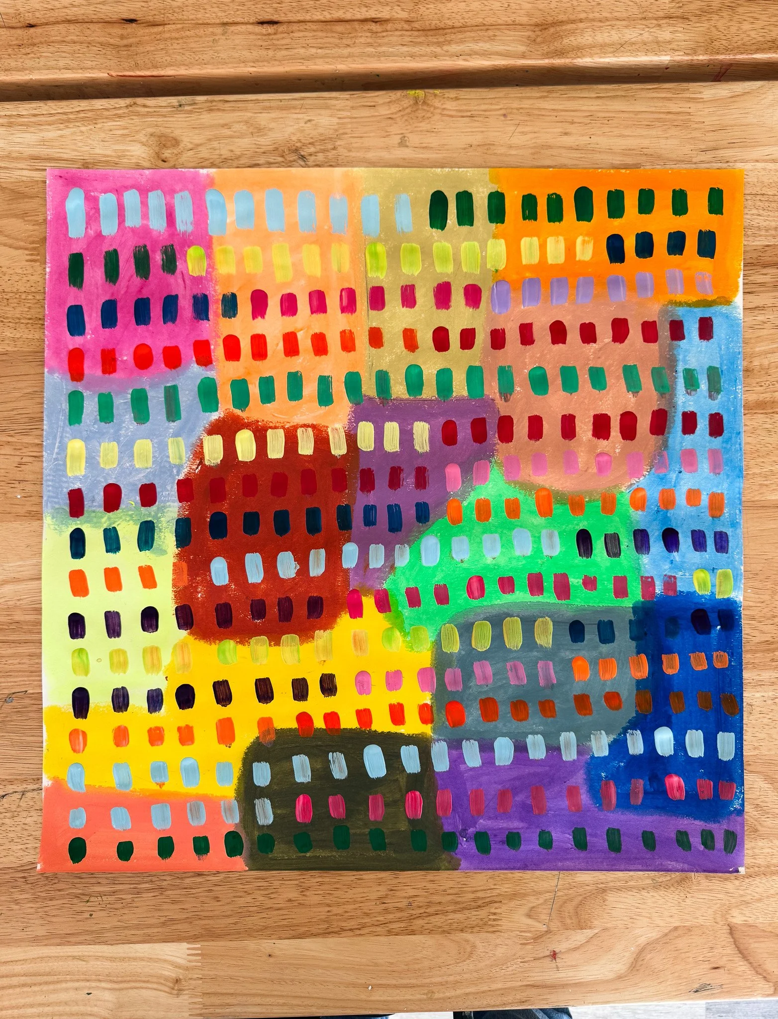 Abstract colorful painting with geometric shapes and squares in pink, orange, yellow, green, purple, and blue on a wooden surface.