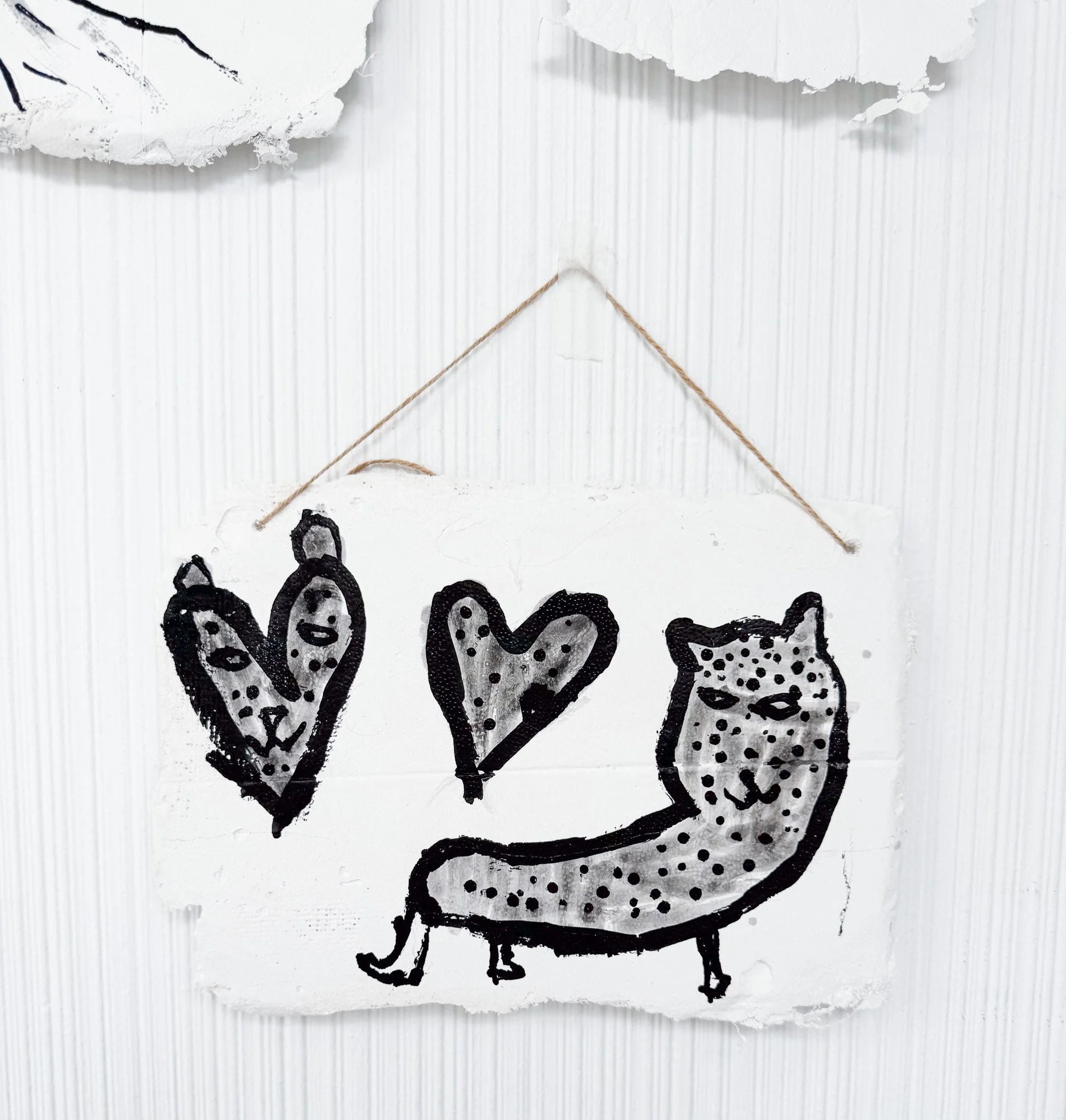 A white sign with black outlines of two smiling hearts and a playful cat with a long body, sitting on its hind legs, decorated with dots.