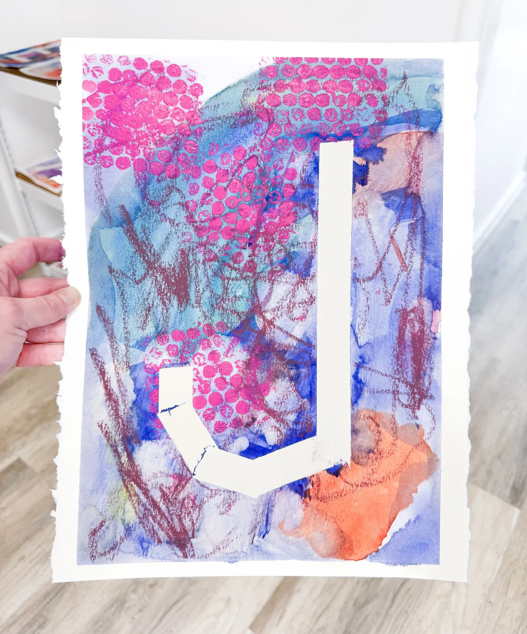An abstract mixed media artwork with blue, purple, pink, and orange watercolor washes, pinprick dots, sketchy lines, and a large white letter 'L' that appears cracked and is overlaid in the center.