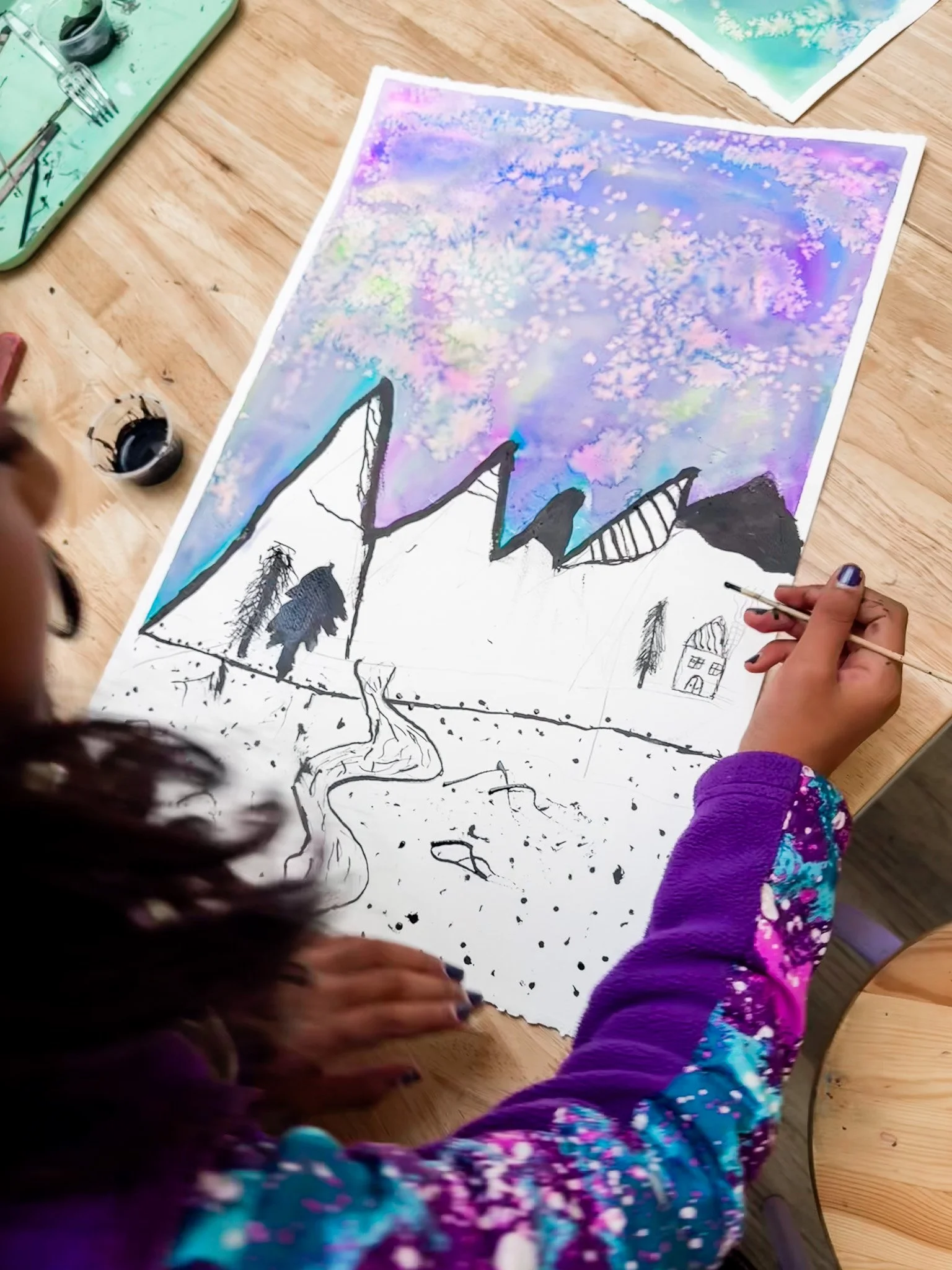 Child painting a mountain landscape on paper with watercolor background.