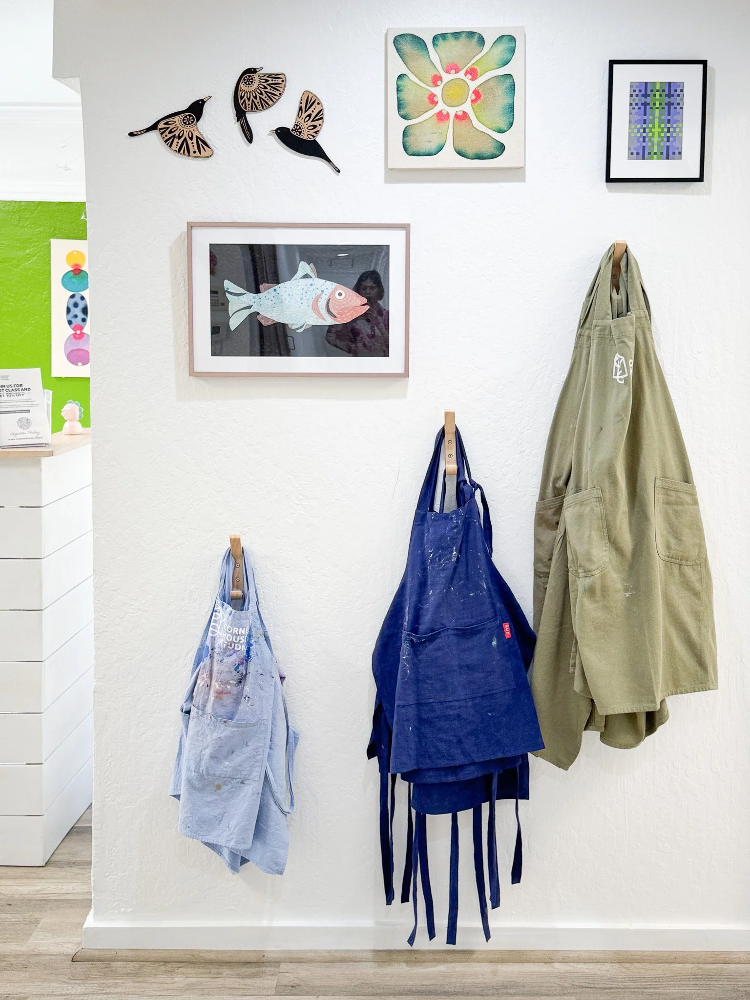 White wall decorated with framed fish and bird artwork, and a couple of hanging aprons or work clothes.