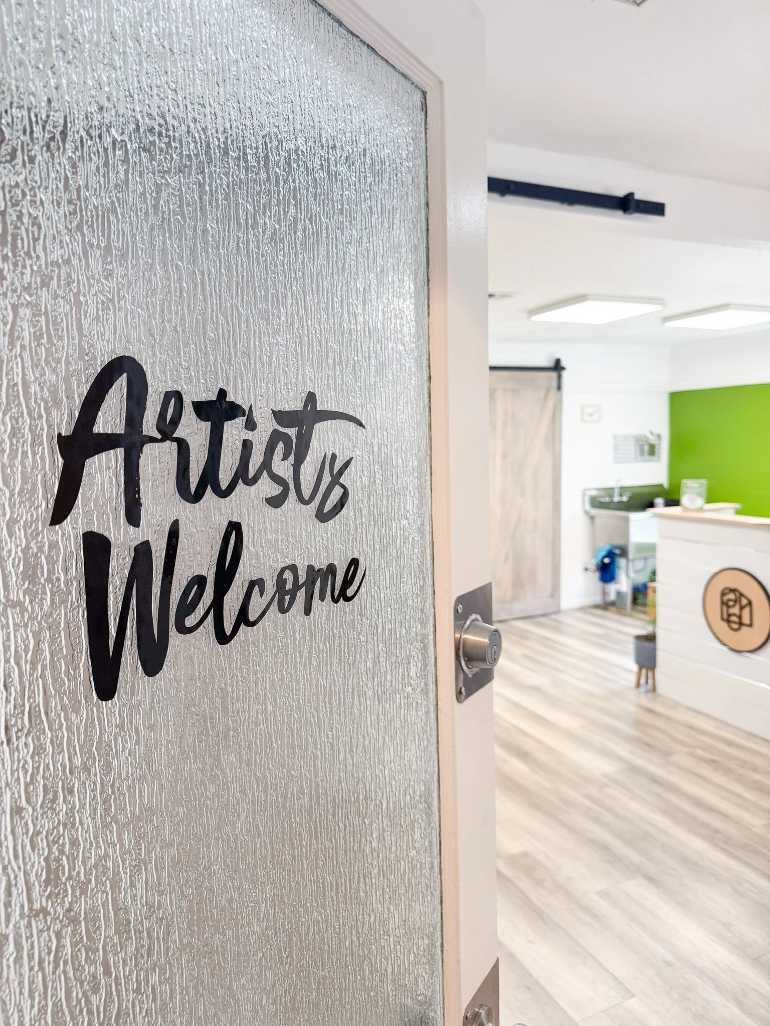A door with a frosted glass window that has the words 'Artist's Welcome' written on it in black cursive font.