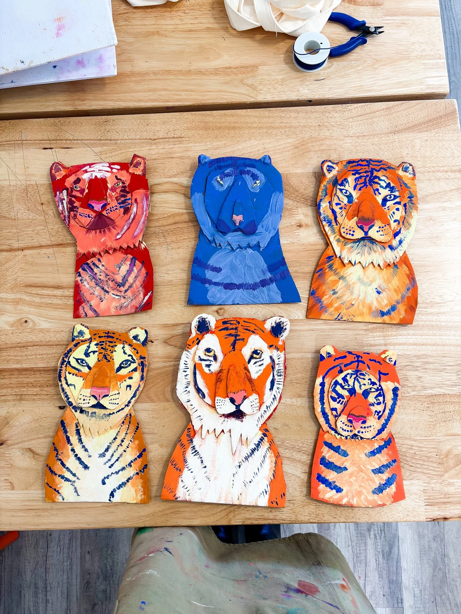 Six colorful paper tiger masks arranged on a wooden table, each painted with different colors and patterns.