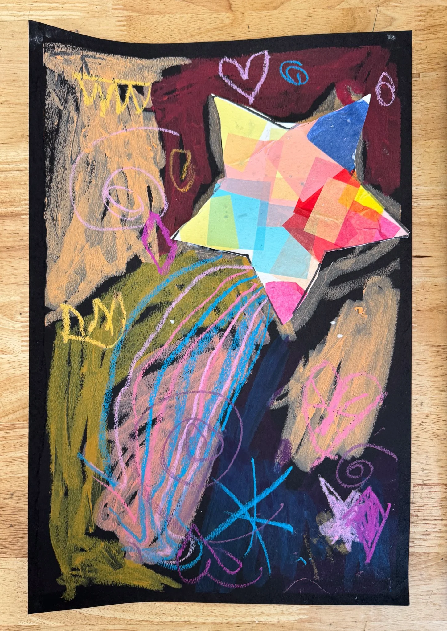 Colorful child's drawing of a star, rainbows, hearts, smiley faces, and other doodles on black paper.