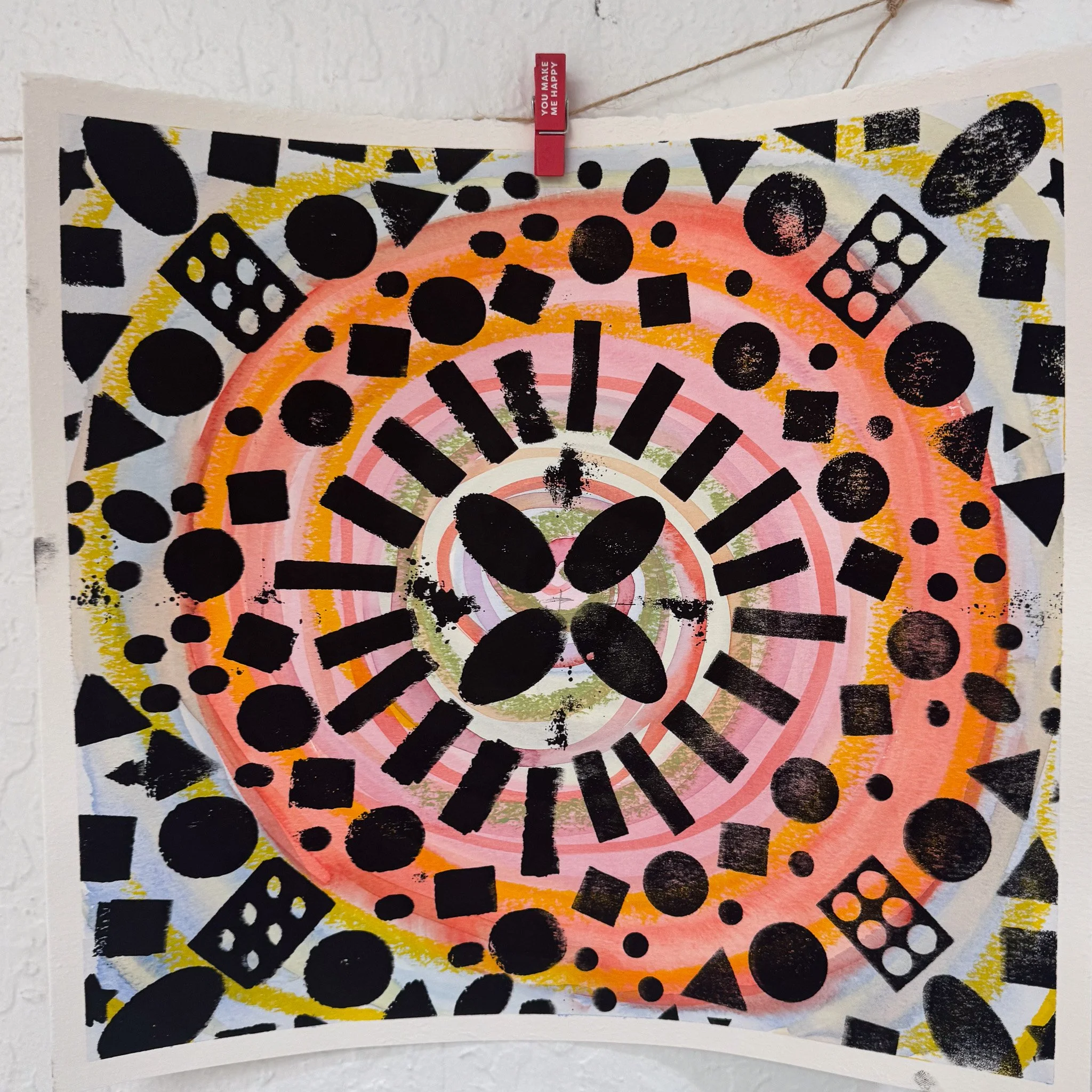 Abstract artwork featuring concentric circles and radiating black geometric shapes including circles, squares, triangles, and rectangles on a white background with yellow, pink, and green accents.