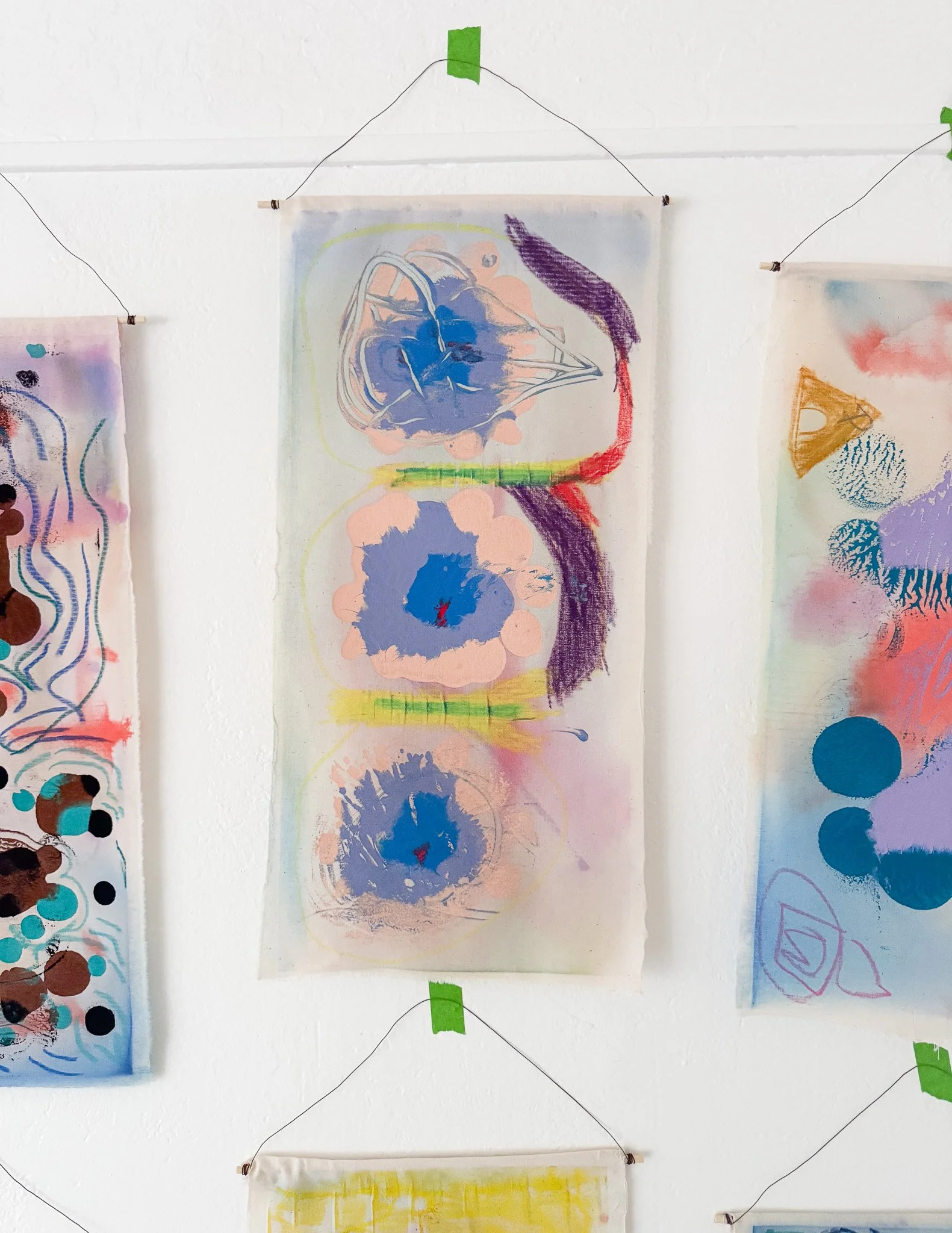 Abstract watercolor artwork featuring three blue circular floral shapes with pink and purple accents, connected by green lines, on a transparent hanging scroll.