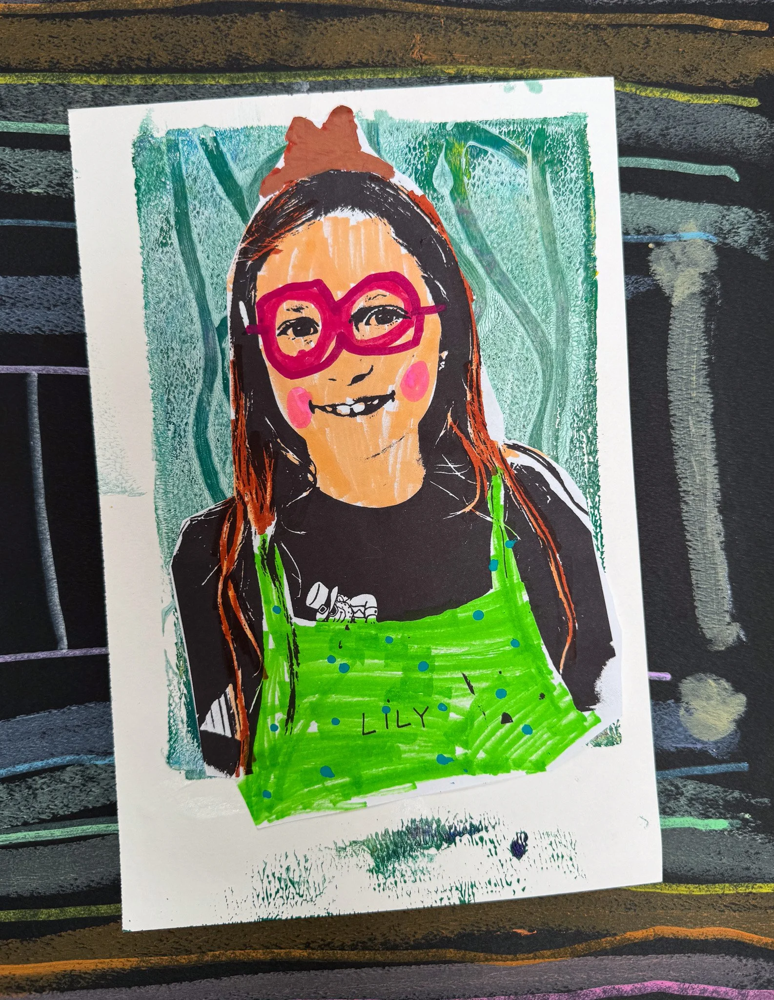 A colorful drawing of a young girl with long brown hair, wearing pink glasses, a black shirt, and a bright green apron. The girl is smiling, showing her teeth, and has pink cheeks. The background features shades of green and teal. The name 'LILY' is 