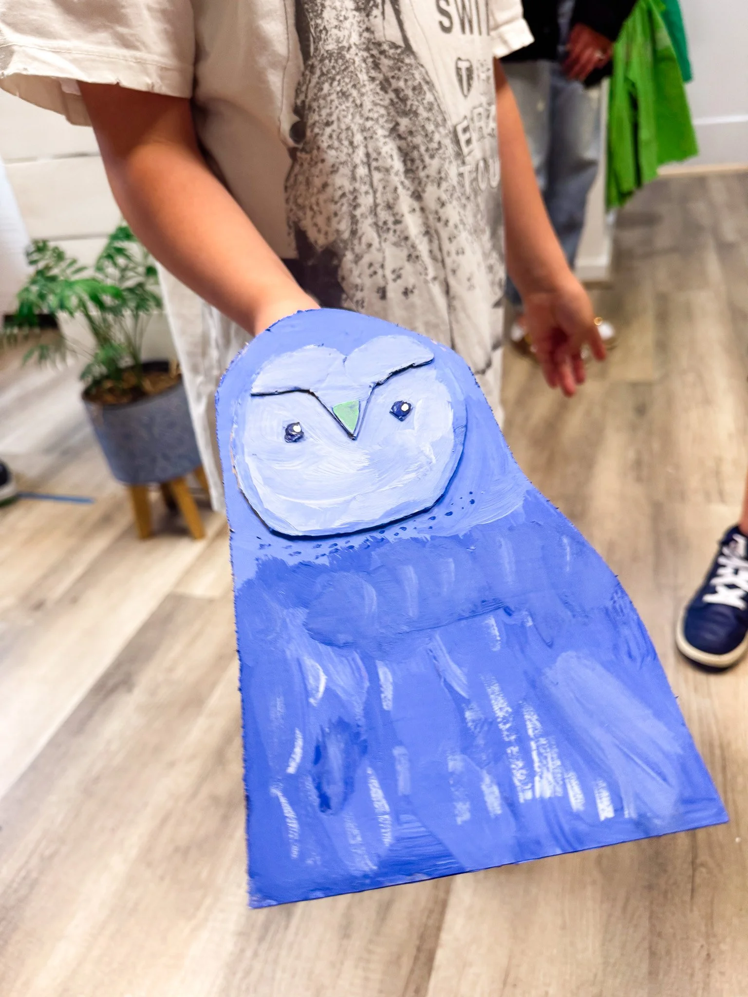 Child holding a blue painted wooden owl craft.