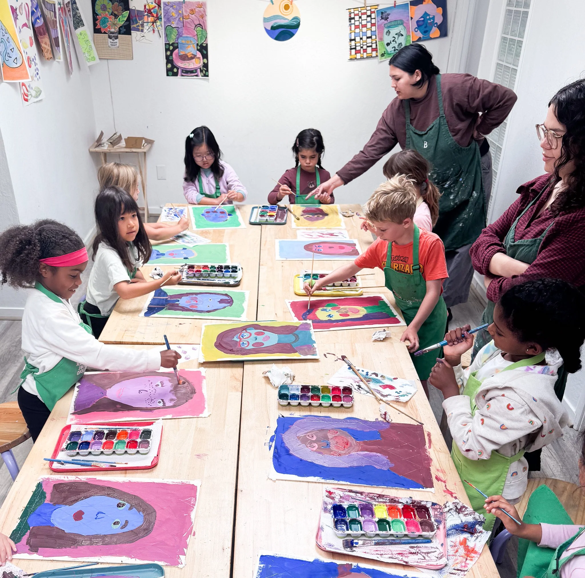 Children in an art class painting colorful self-portraits while teachers supervise.