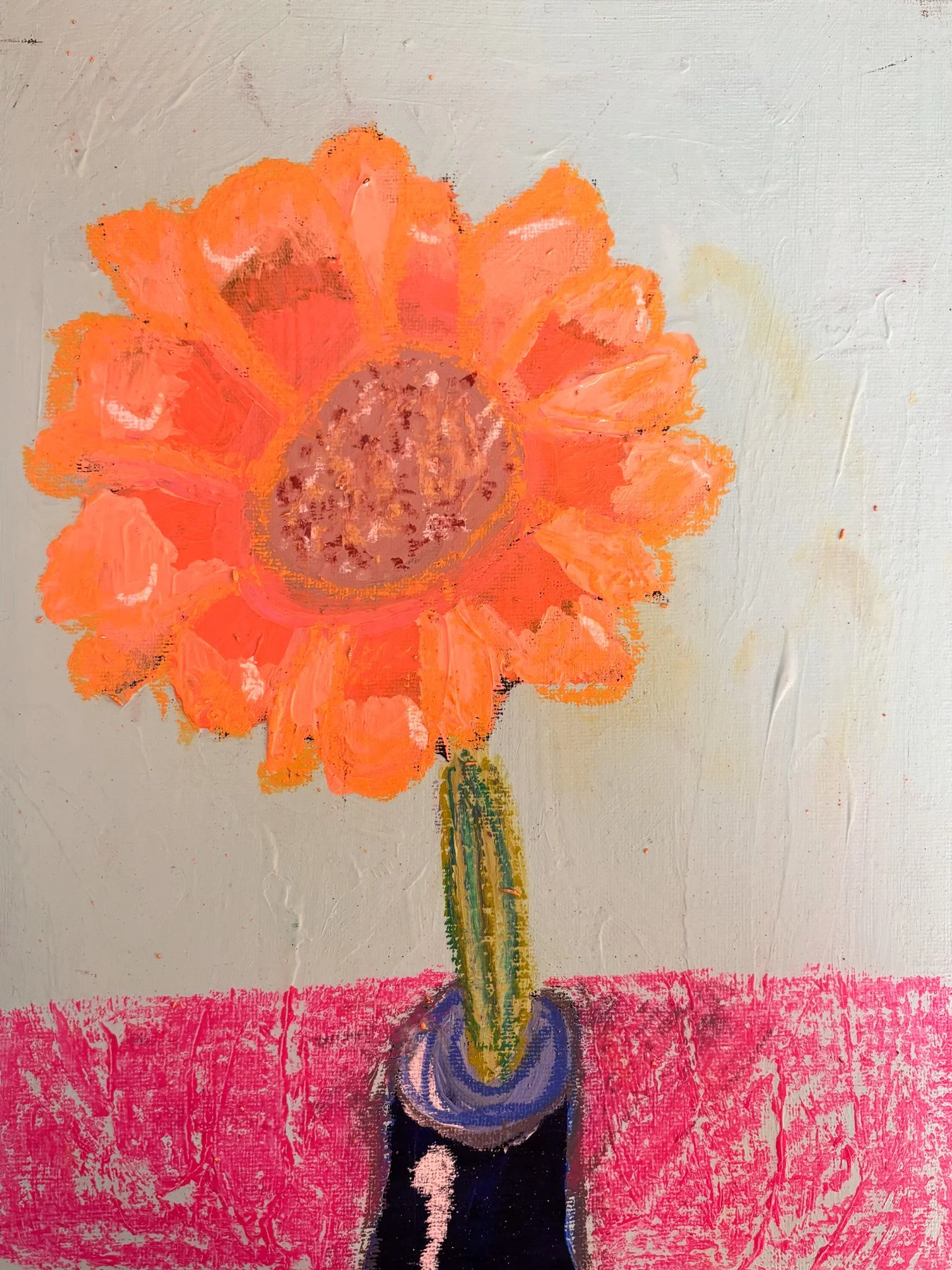 A bright orange flower in a purple vase. The flower has multiple petals, and the background is gray with a pink surface underneath the vase.