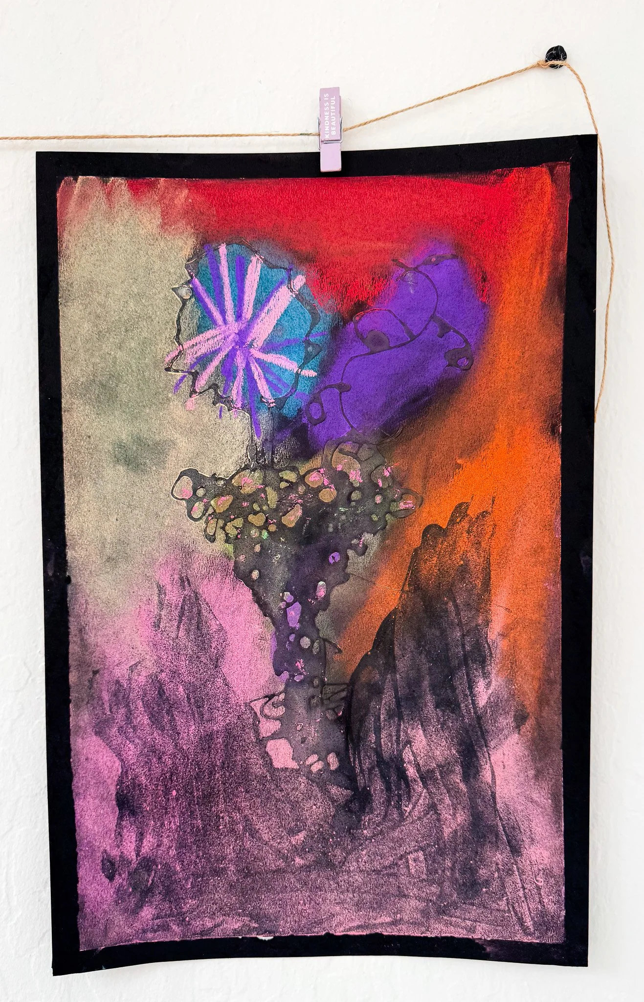 Abstract artwork with vibrant colors, including purple, red, orange, black, and pink, featuring shapes like a flower and a butterfly, displayed on a wall with a string and clip.